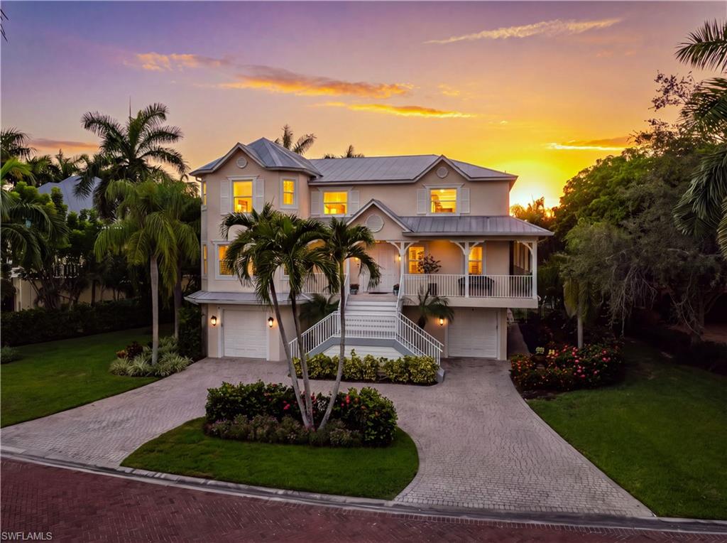 Two-story coastal-style home with a raised porch and palm trees at sunset.