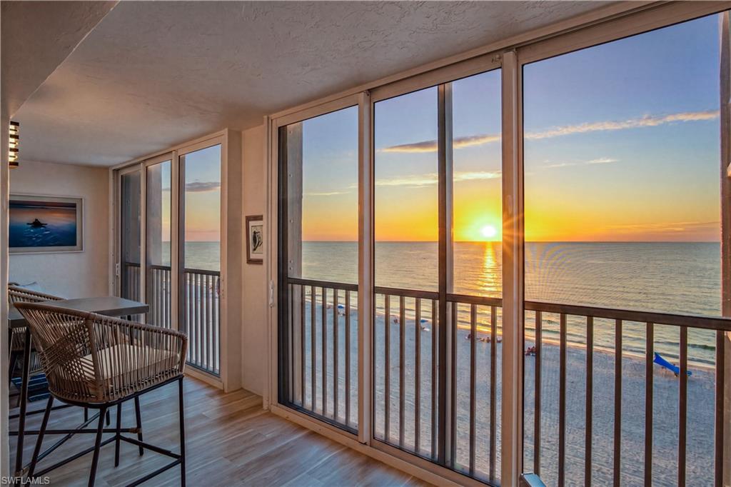 Condo dining area overlooking the beach and ocean through sliding glass doors at sunset.