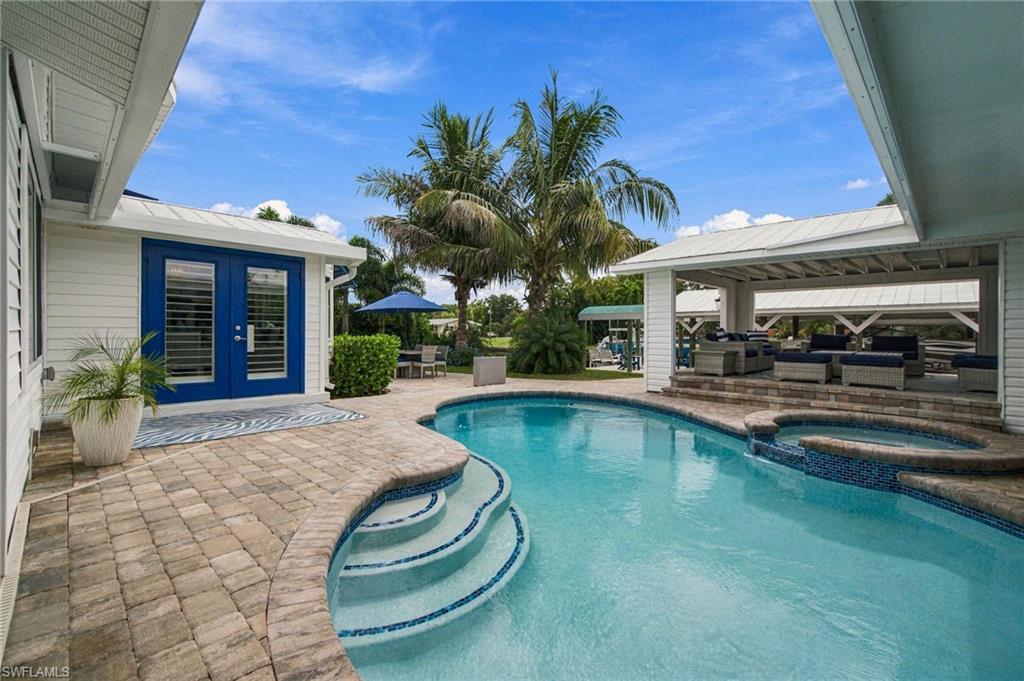 Courtyard pool with curved tiled steps, blue double doors, palms, and covered patio seating.