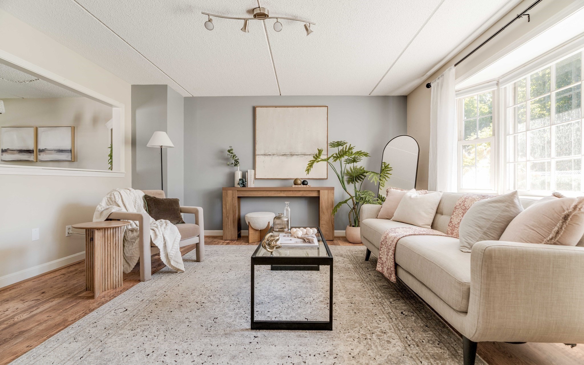 Staged living room with a cream sofa, wood console, gray accent wall, and large bright windows.