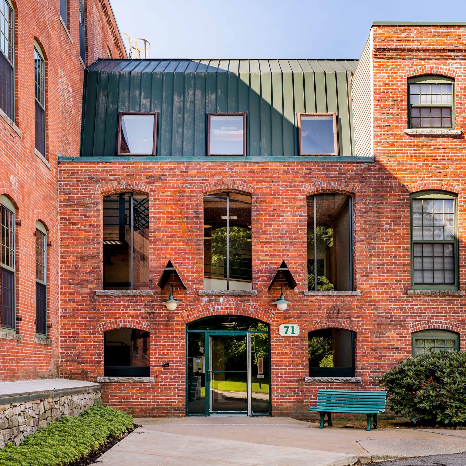 Red-brick building with a green metal upper story, arched windows, and a glass entrance marked 71.