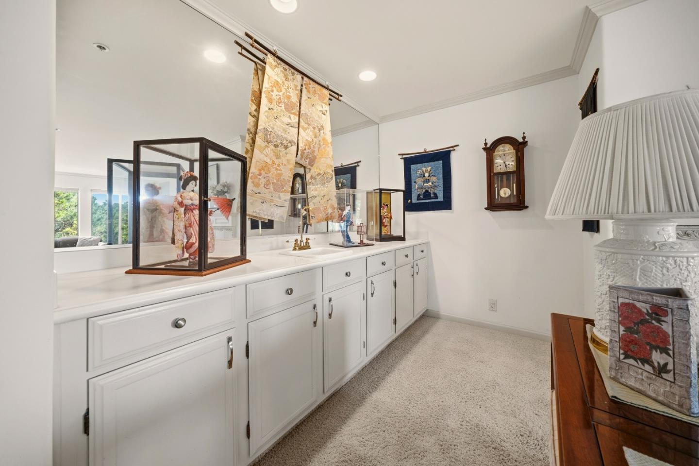 Carpeted room with white built-in cabinets, mirrored counter, collectible displays, and a large table lamp.
