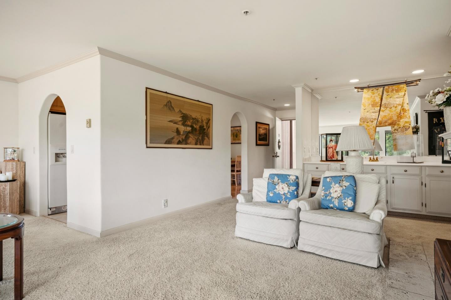 Living room with white sofas, blue floral pillows, beige carpet, and arched openings.