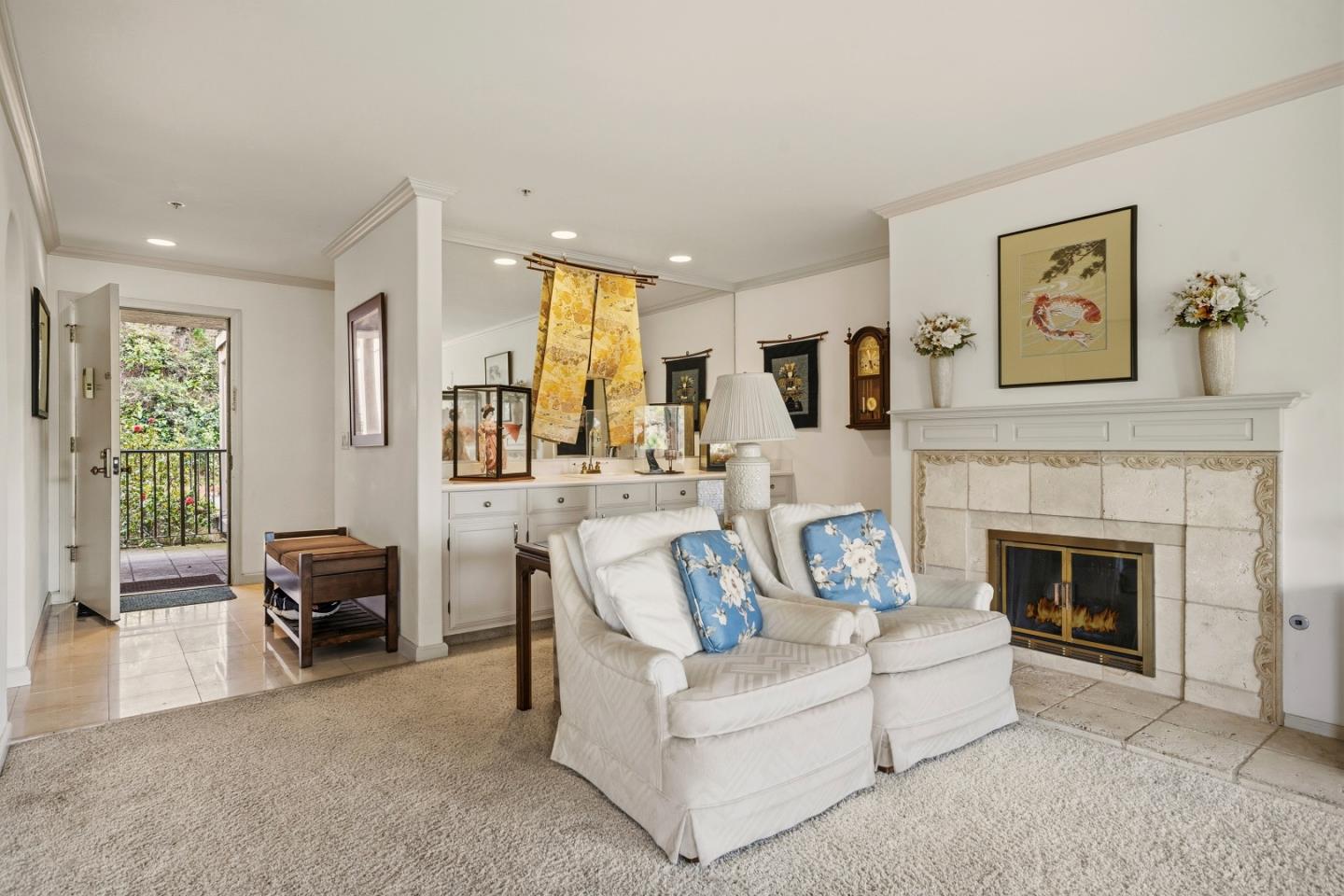 Living room with a stone fireplace, white sofa, blue floral pillows, and an open door to a garden patio.