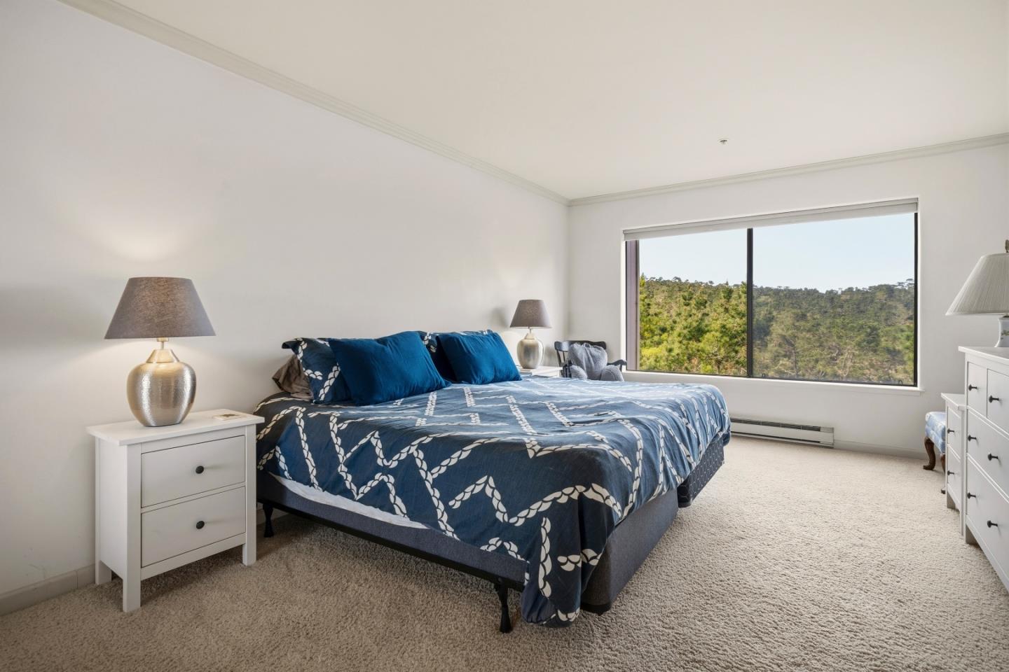 Bedroom with blue patterned bedding and a wide window overlooking wooded hills.