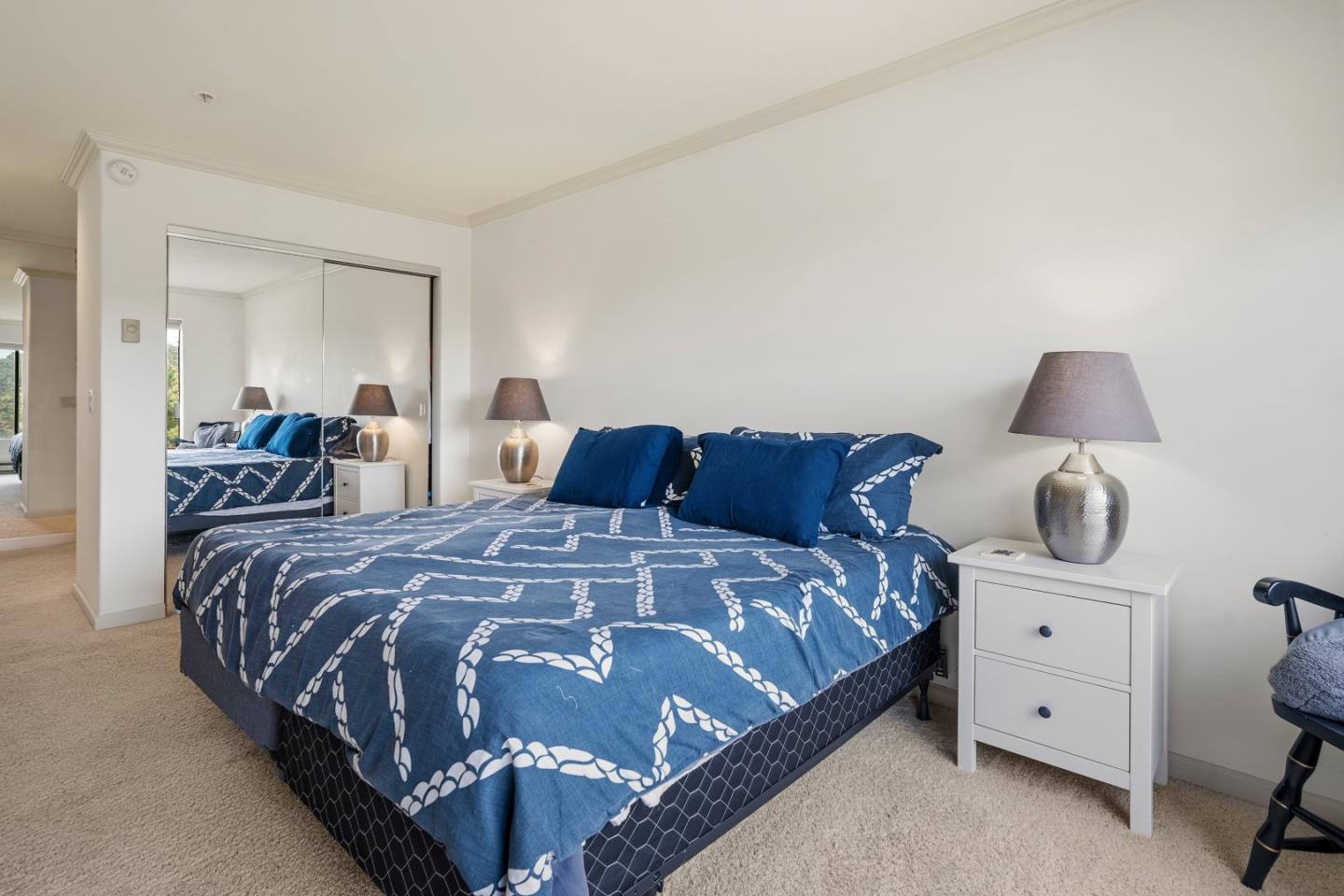 Bedroom with blue patterned bedding, mirrored closet doors, and white bedside tables.