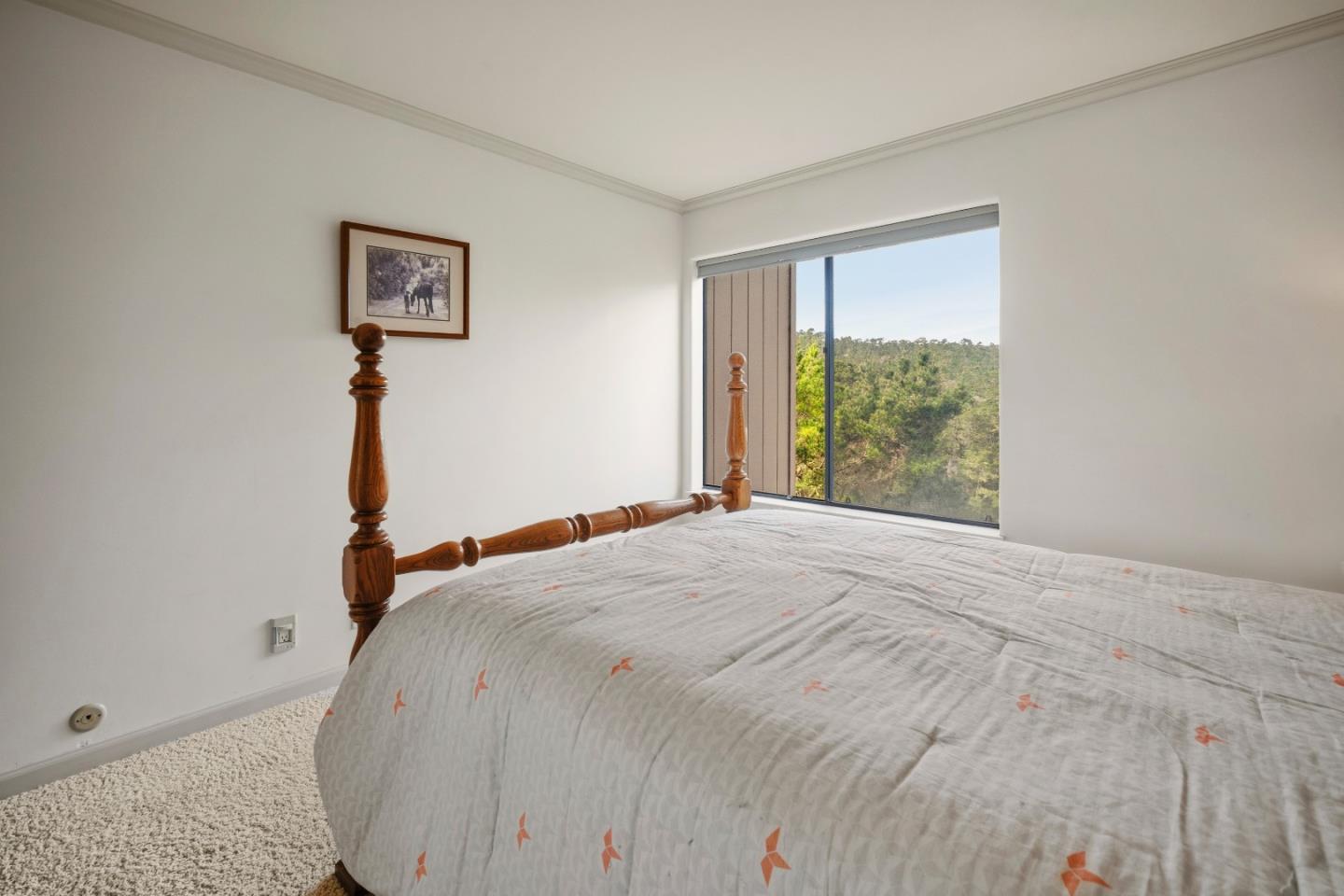 Bedroom with a carved wooden bed, patterned white quilt, and window overlooking a wooded hillside.