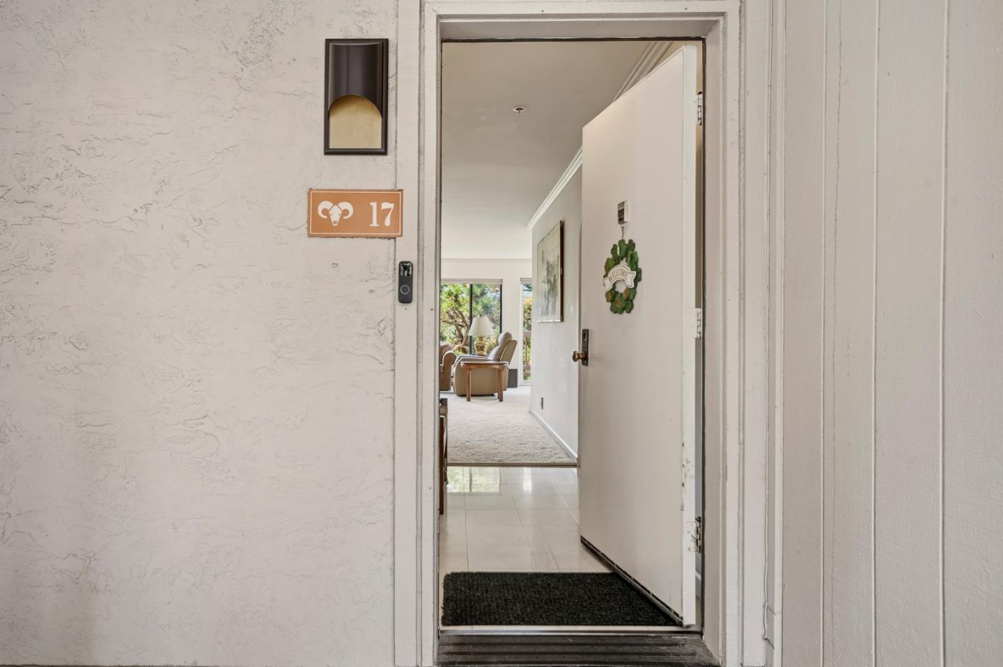 Open front door reveals a tiled entry and furnished living room with large windows beyond.
