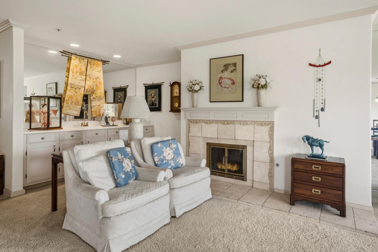 Living room with white sofas and blue floral pillows beside a pale stone fireplace.