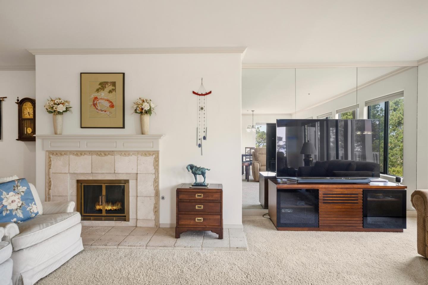 Living room with a stone fireplace, white sofa, and television beside mirrored panels and bright windows.