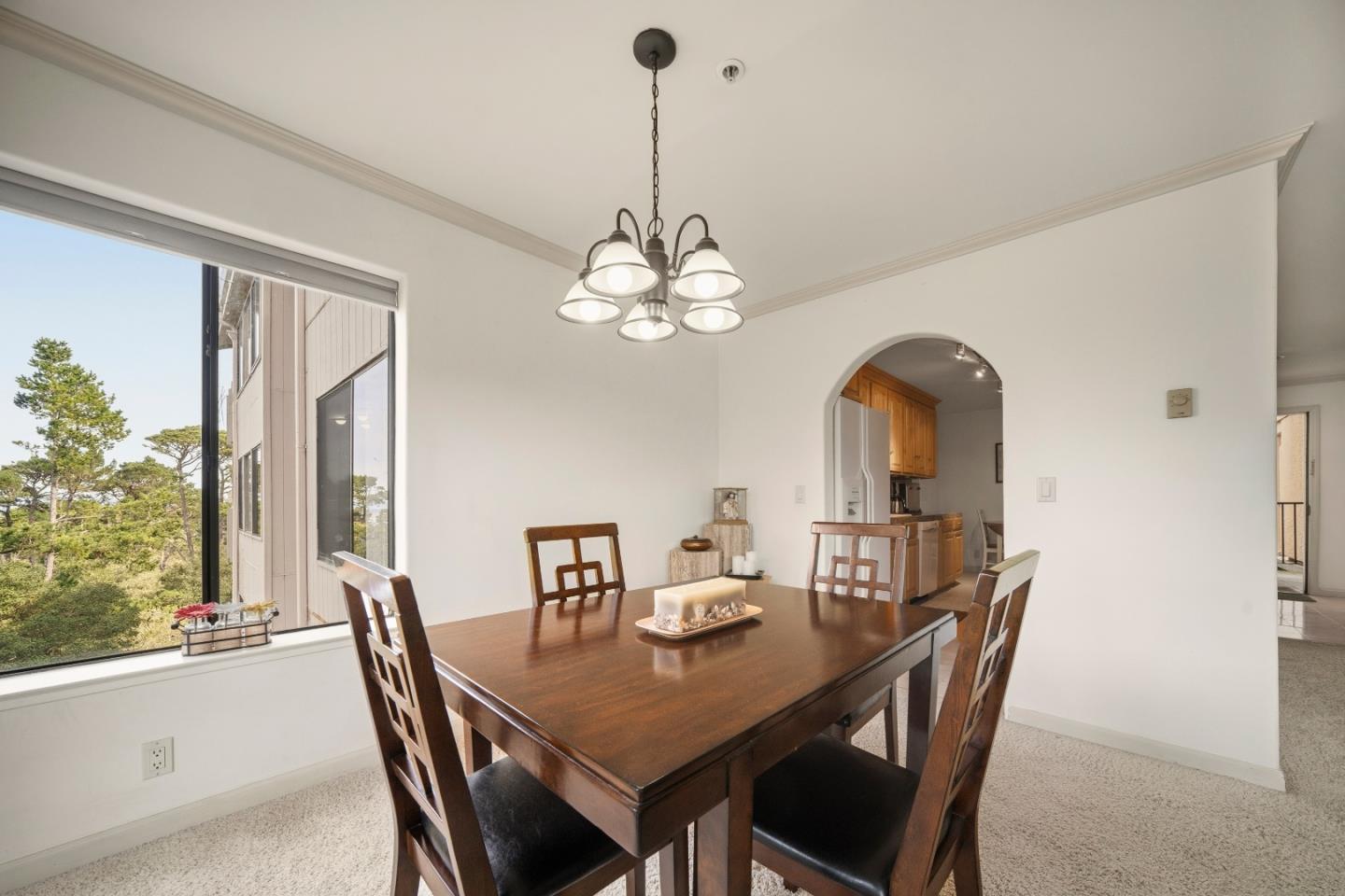 Dining room with a dark wood table, chandelier, and large window overlooking trees.