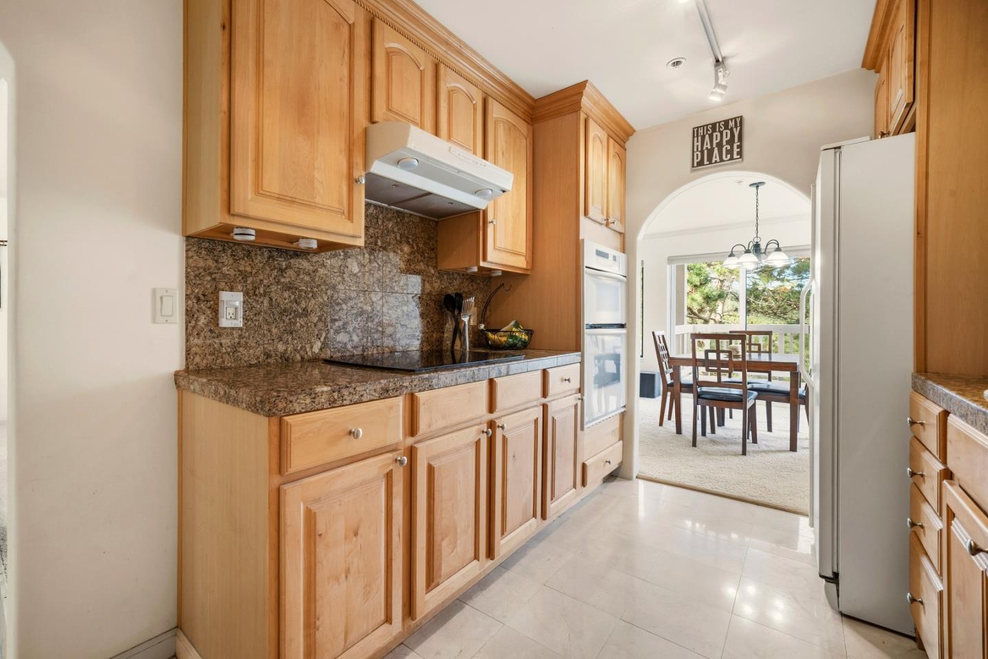 Kitchen with wood cabinetry and granite counters, opening through an arch to a dining area.