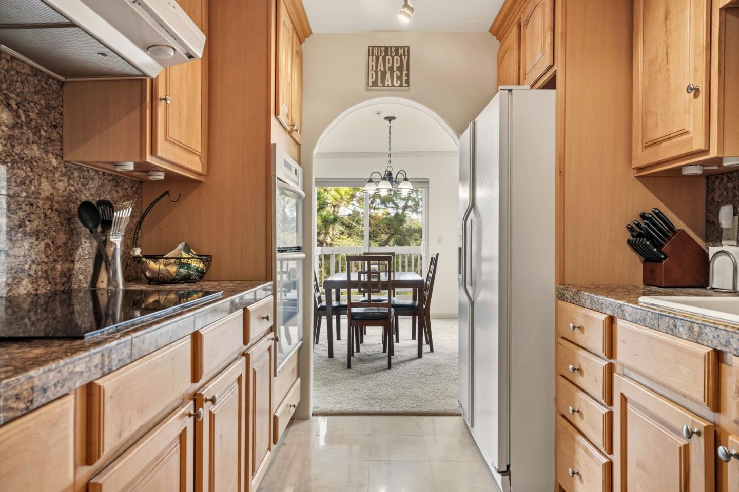 Kitchen with wood cabinets and granite counters opening to a dining nook beneath an arched doorway.