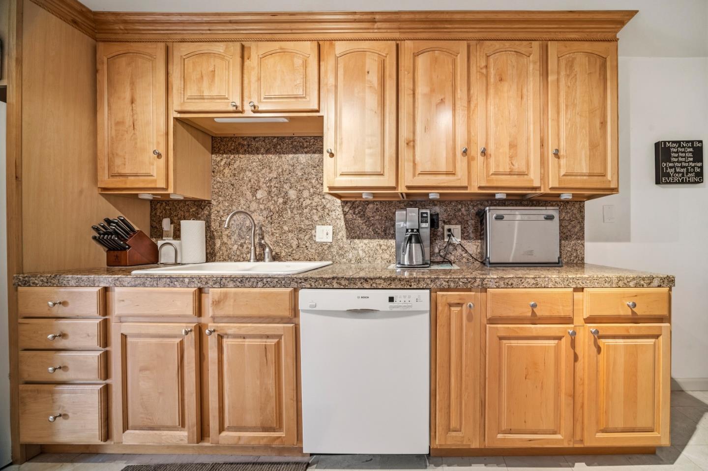 Kitchen with light wood cabinets, granite counters and backsplash, white sink, and dishwasher.