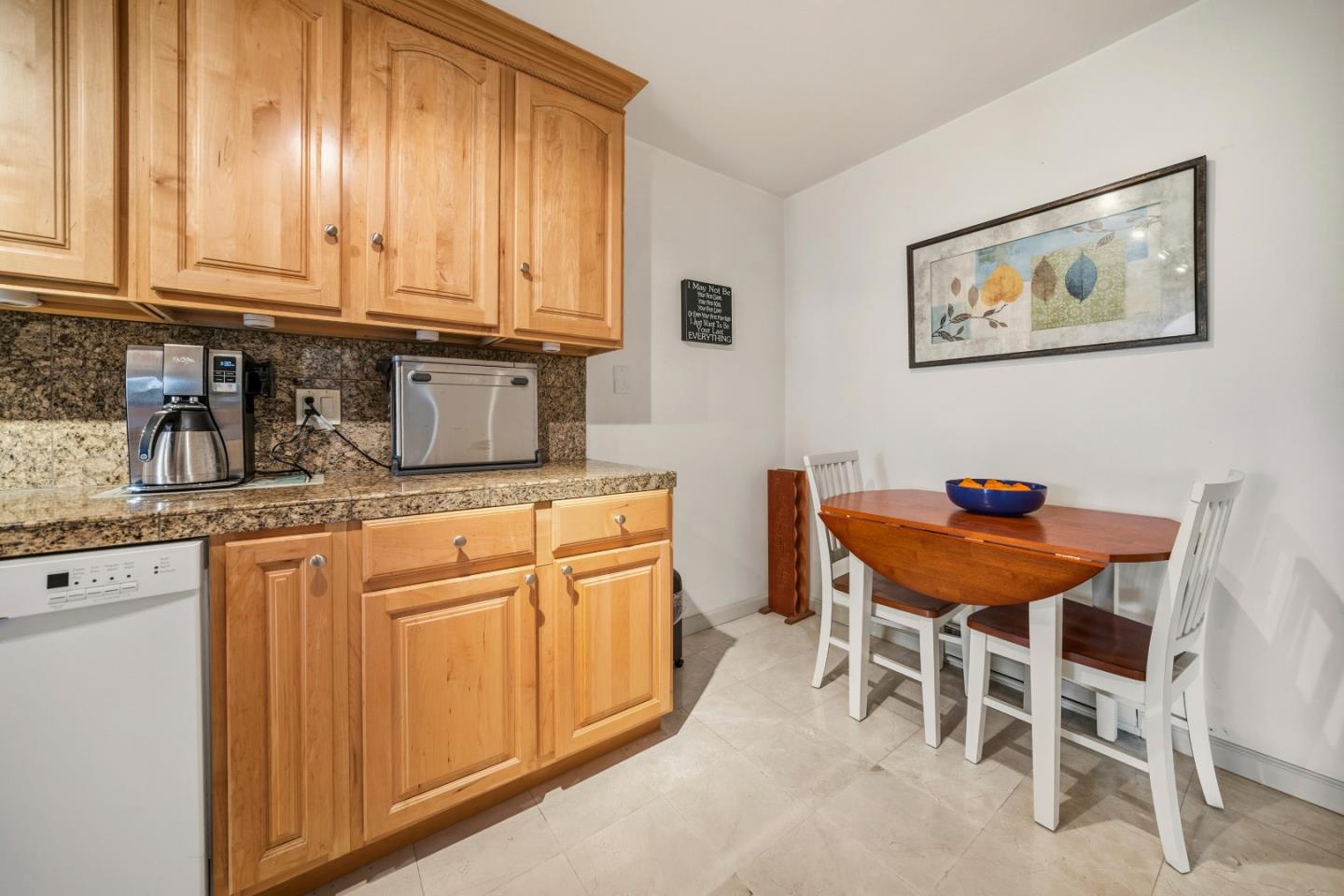 Kitchen and dining nook with wood cabinets, granite counters, and a round table with white chairs.