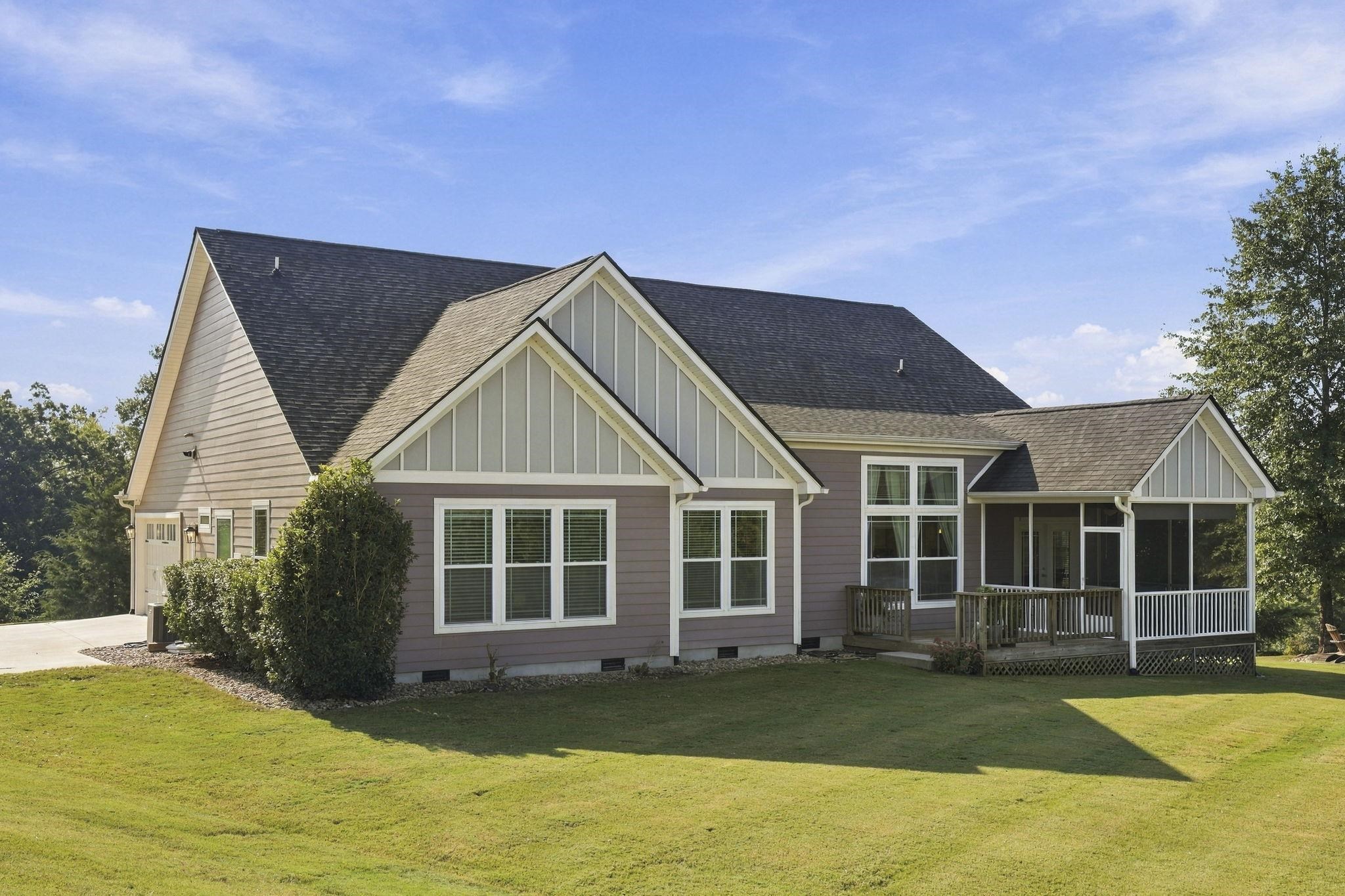 Gray-sided home with prominent gables and a covered screened porch overlooking a broad lawn.
