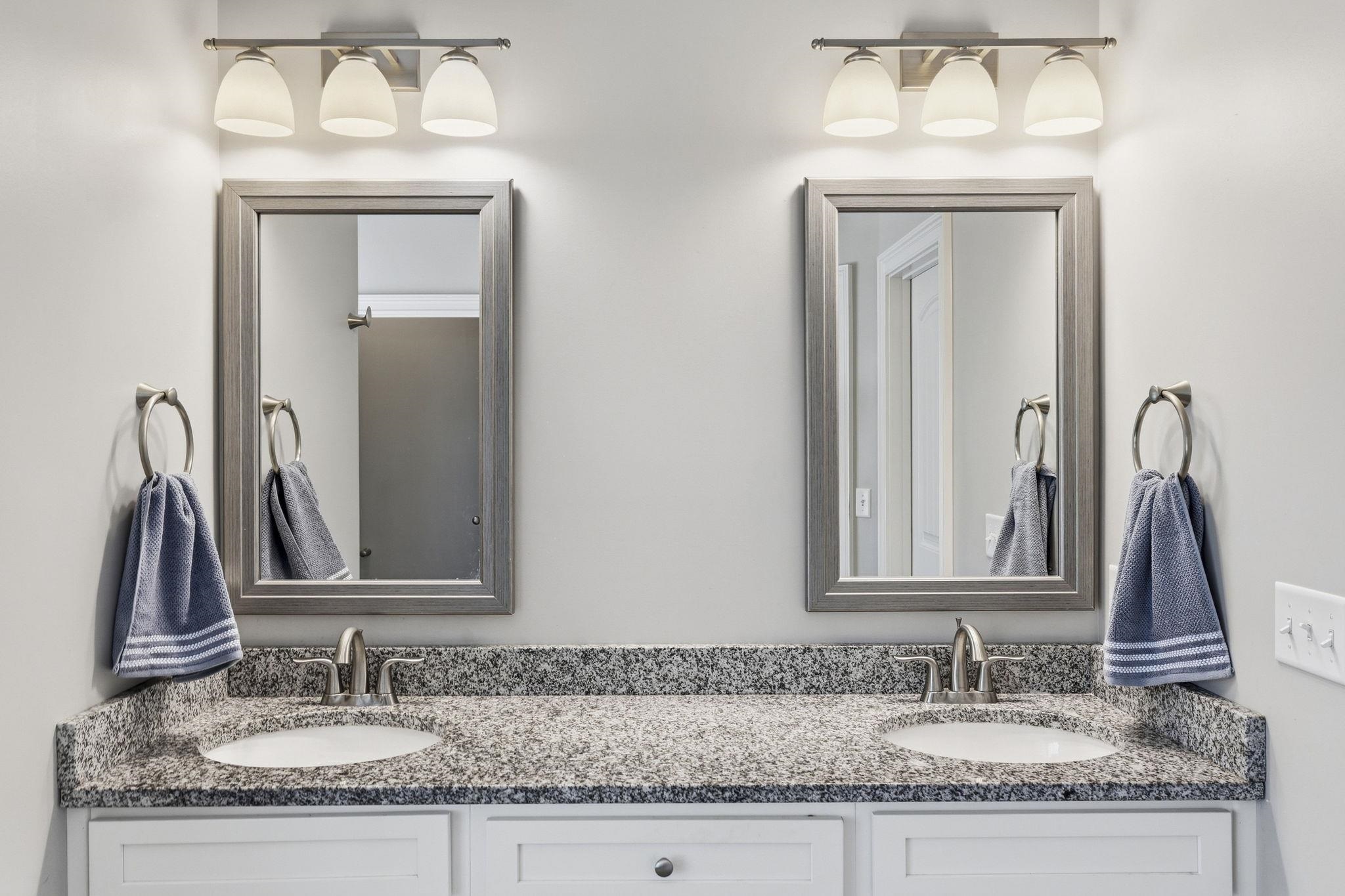Bathroom double vanity with speckled granite countertop, two sinks, framed mirrors, and blue-gray towels.
