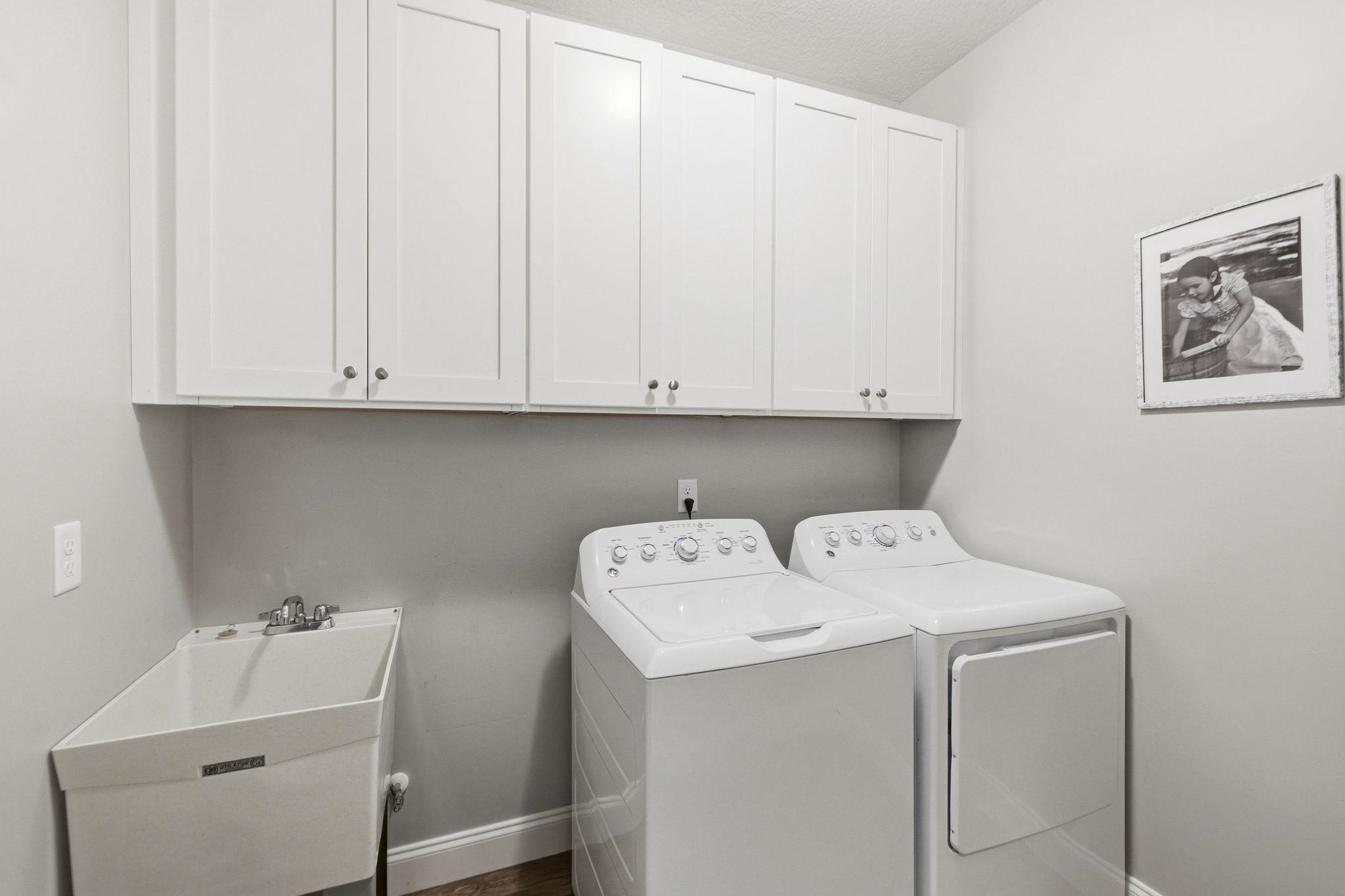 Laundry room with white cabinets, a utility sink, and a washer and dryer.