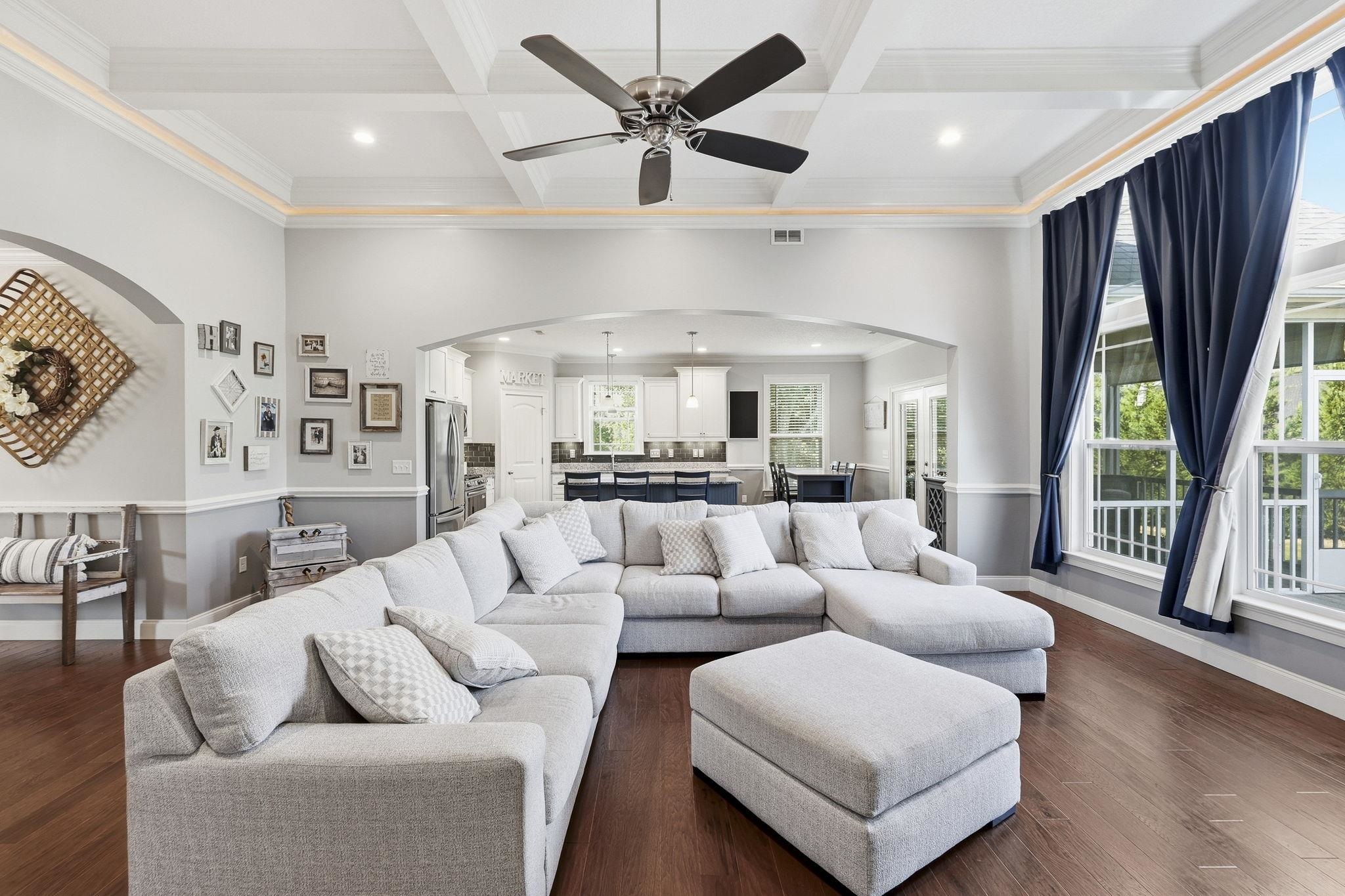 Open-plan living room with a large gray sectional, navy curtains, and a kitchen beyond.