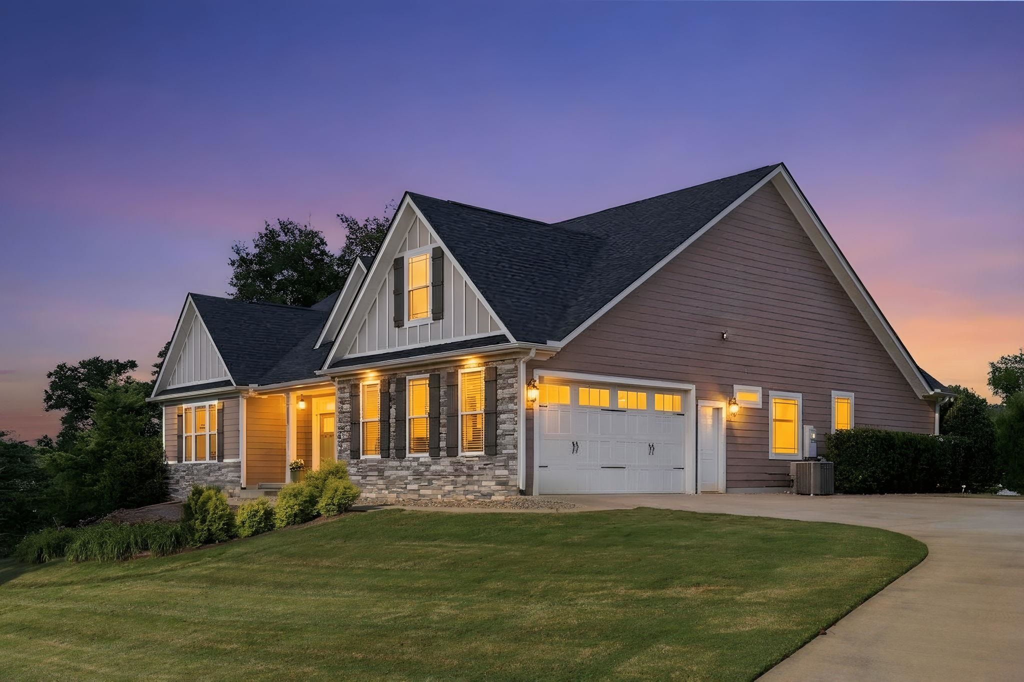 Gabled house with a stone facade and glowing windows at dusk.