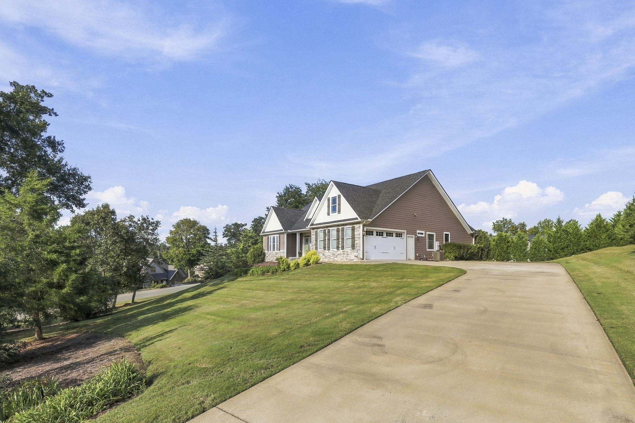 House with stone accents and attached garage beside a curved driveway and sloped lawn.