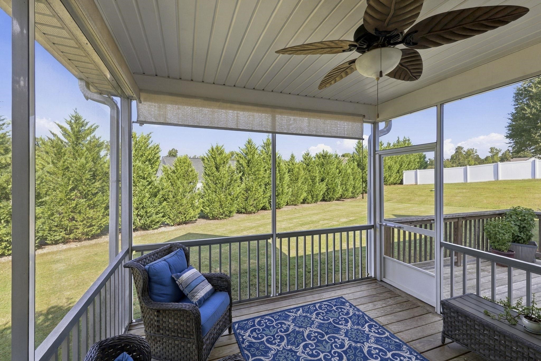 Screened porch with wicker seating, blue cushions, ceiling fan, and a fenced yard view.