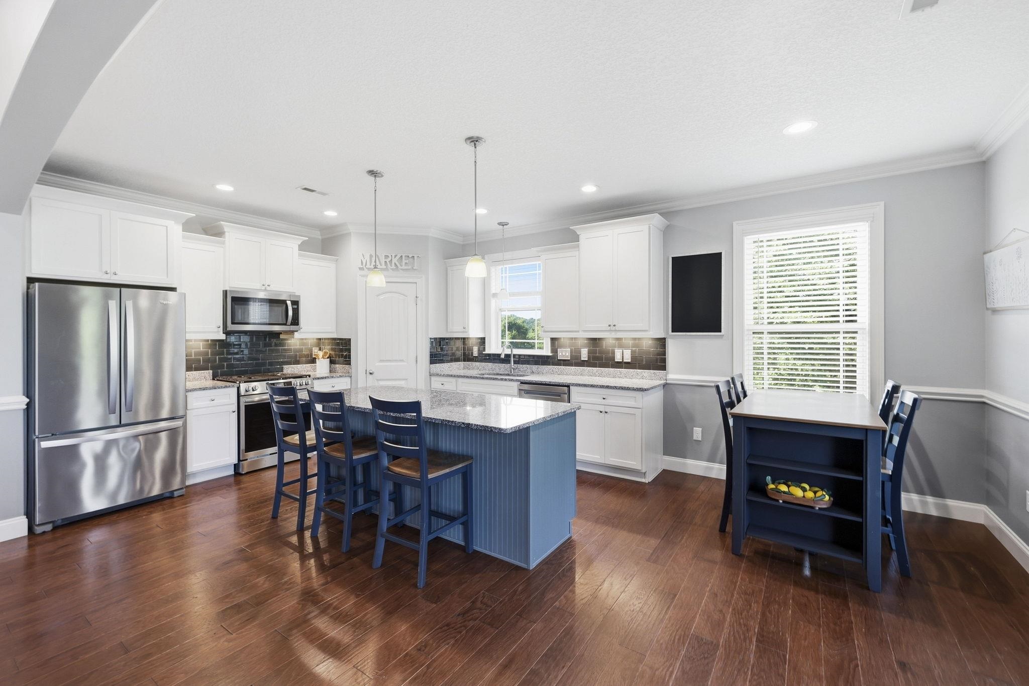 Kitchen with white cabinets, stainless steel appliances, and a blue island beside a dining table.