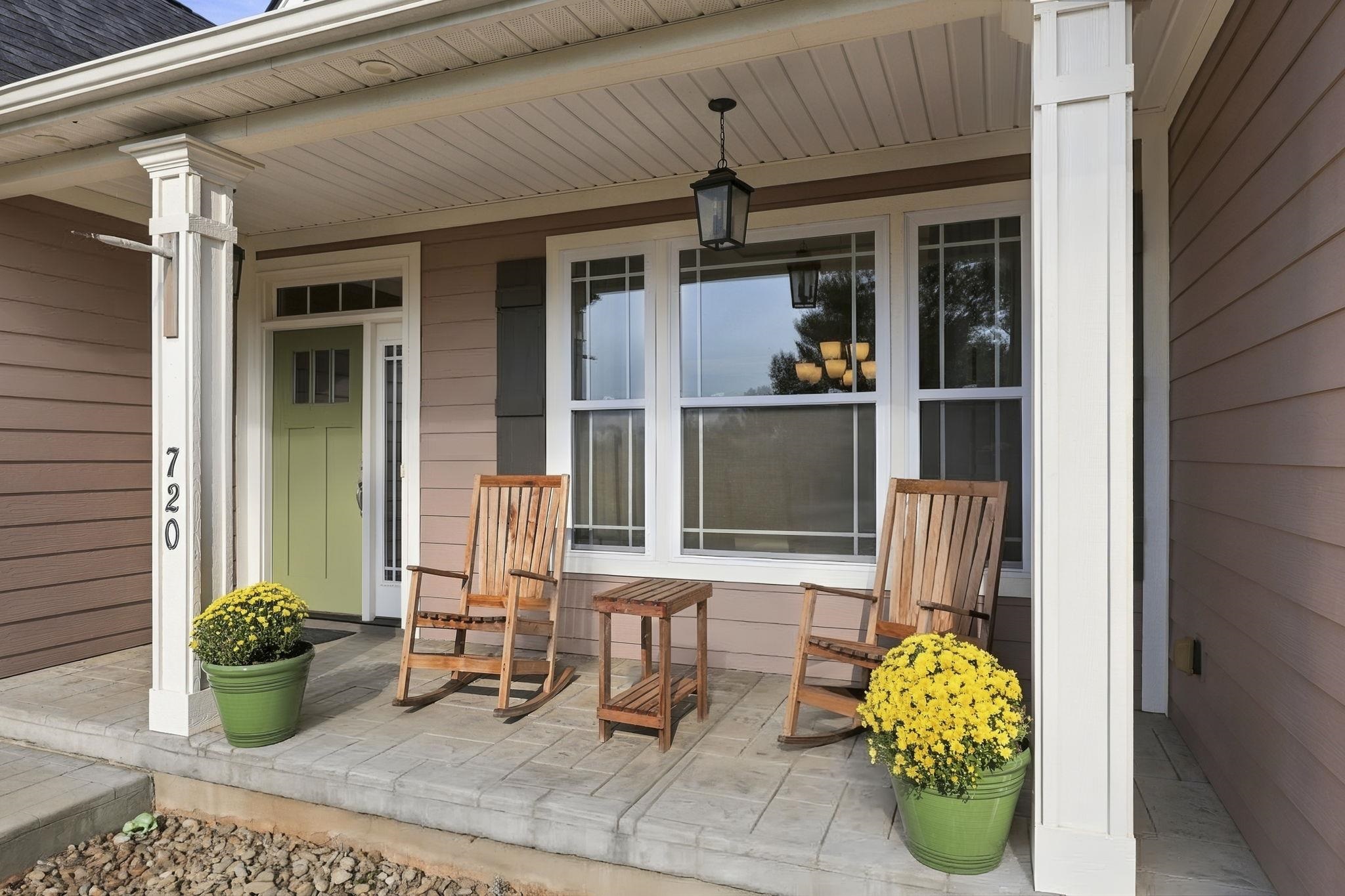 Covered front porch with rocking chairs, a green entry door, and potted yellow chrysanthemums.