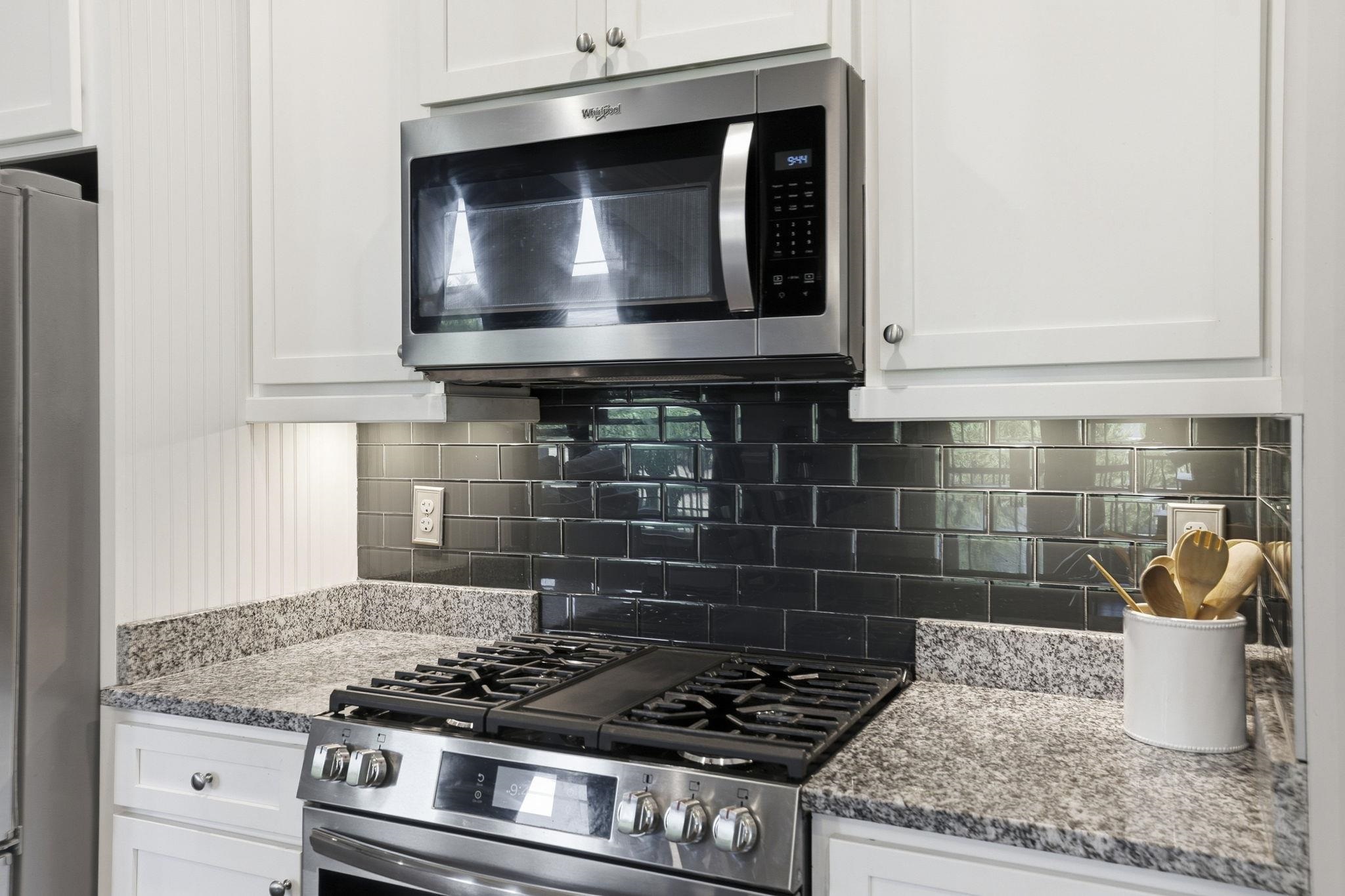 Kitchen range and microwave against a glossy dark tile backsplash with granite counters.