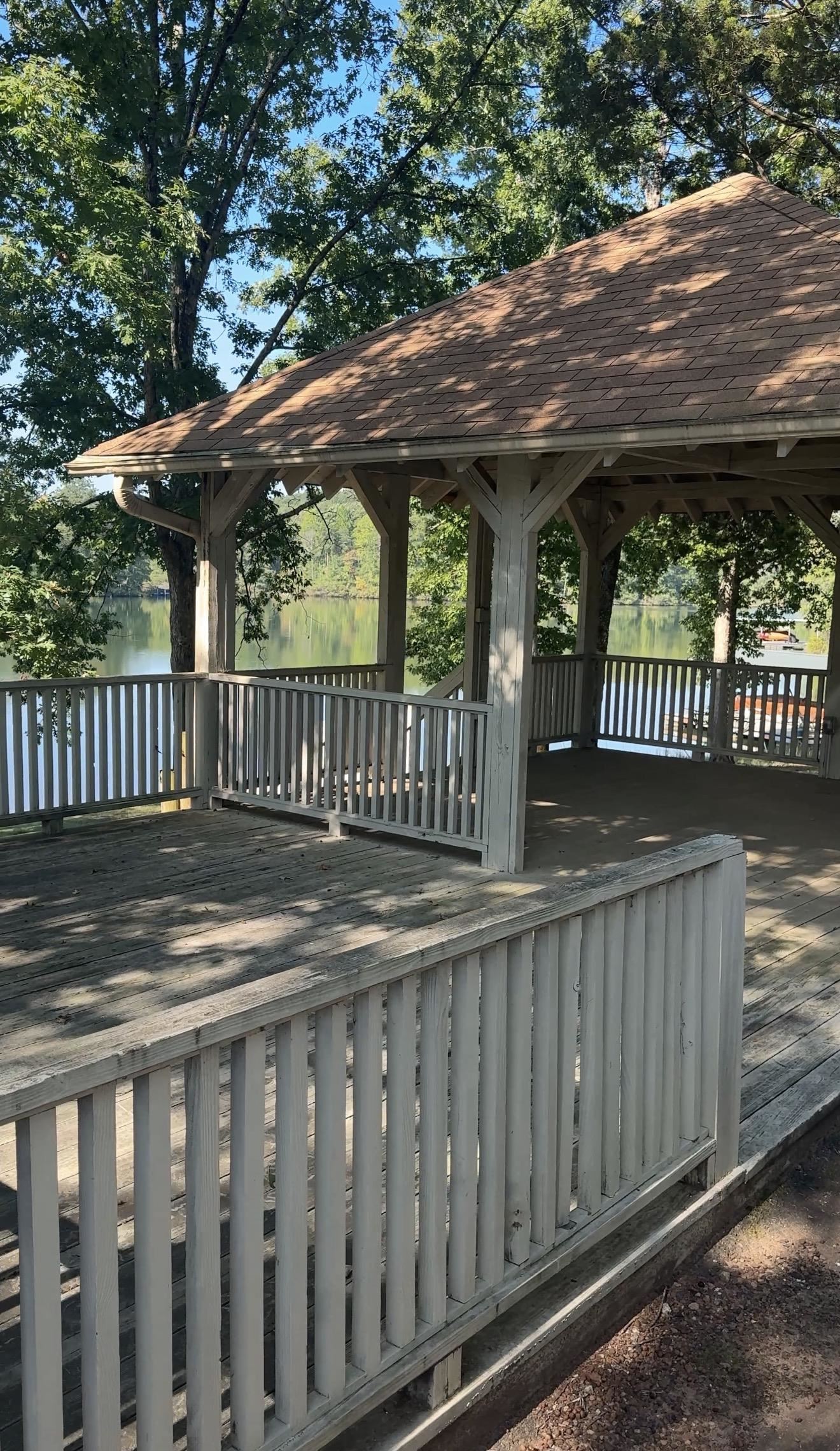 Covered wooden pavilion and weathered deck overlooking a lake through mature trees.