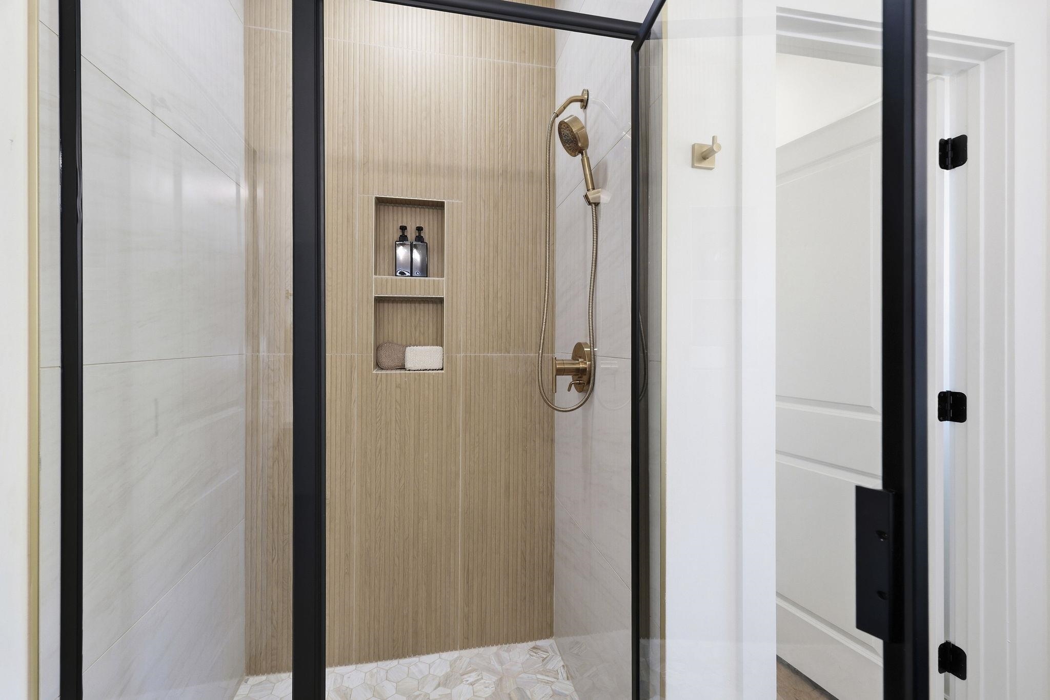 Walk-in shower with a wood-look accent wall, recessed niches, and brass fixtures.