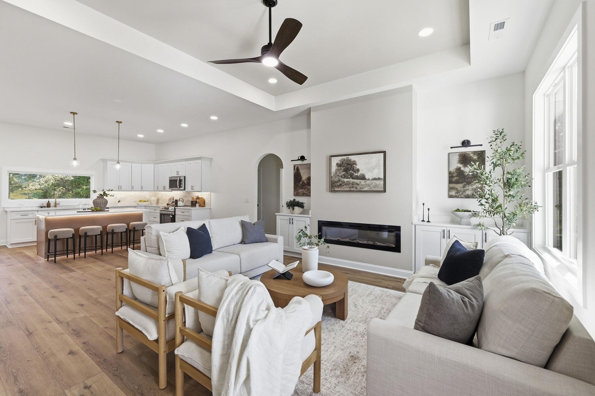Open-concept living room and kitchen with a fireplace, white sofas, and a breakfast bar.