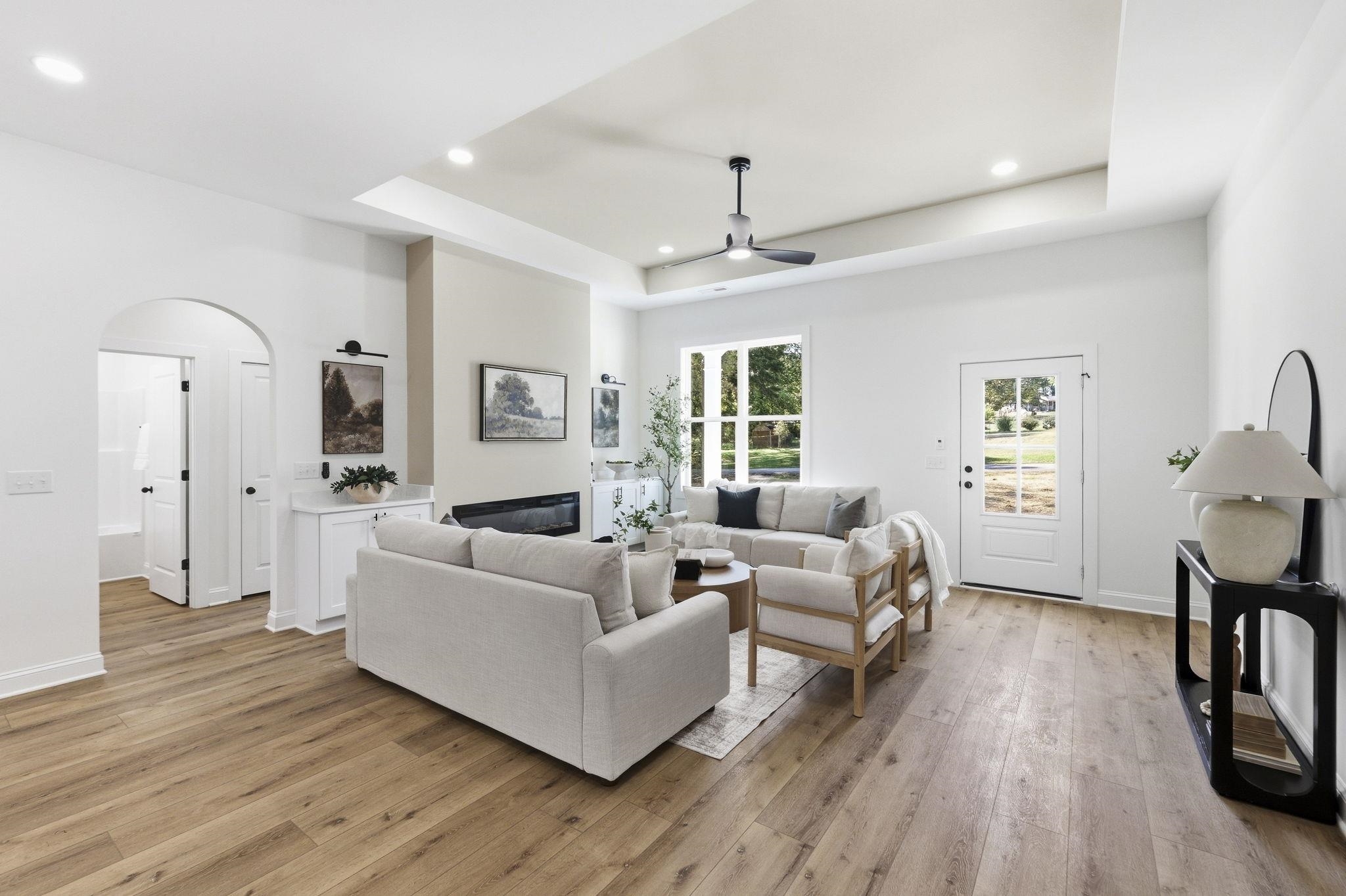 Bright living room with neutral seating, a linear fireplace, warm wood floors, and a tray ceiling.