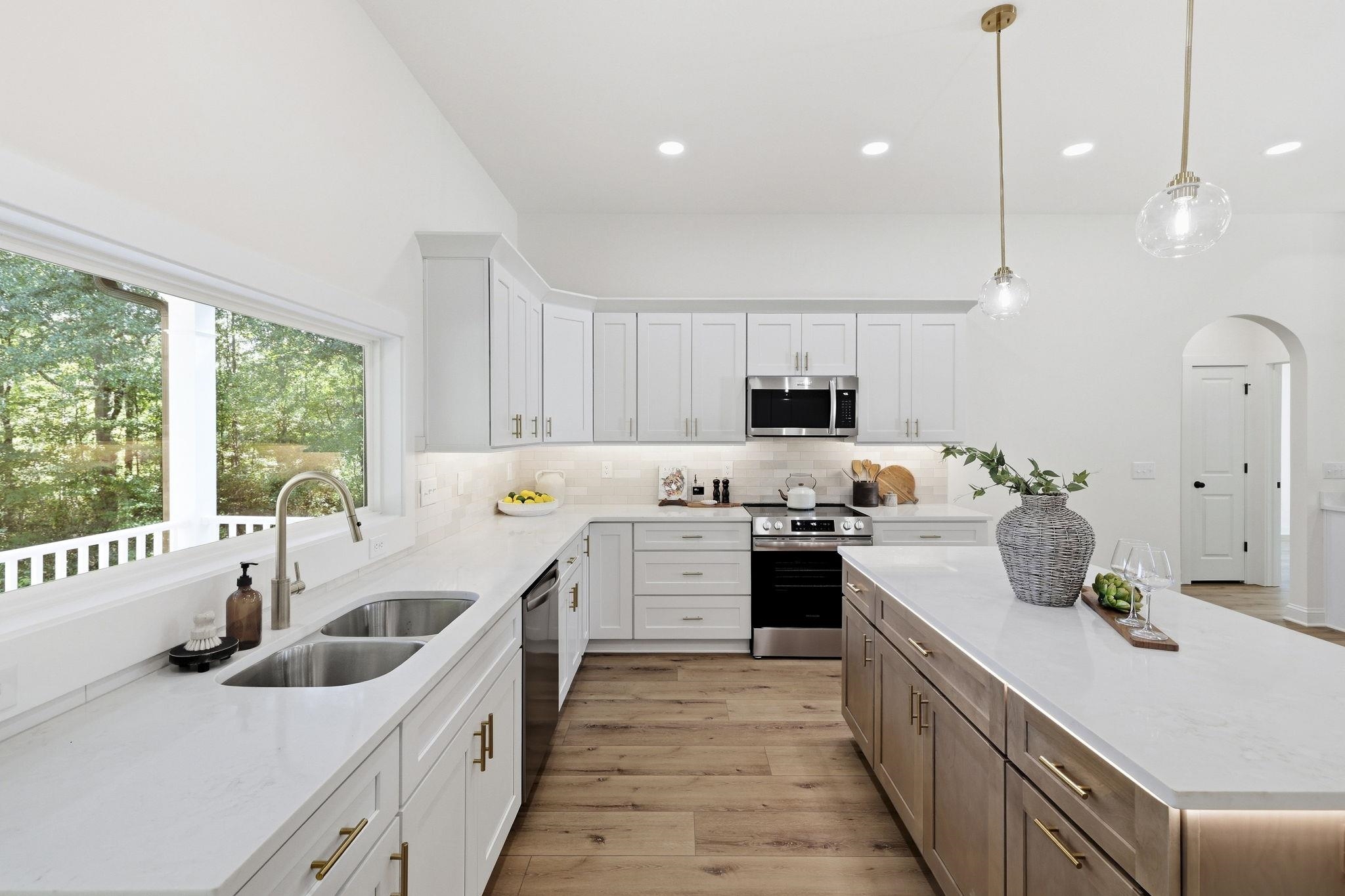 Bright kitchen with white cabinets, a large island, stainless steel appliances, and a window overlooking trees.