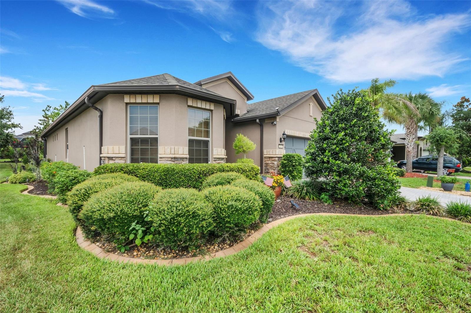 Beige stucco home with stone accents, a garage, and landscaped front yard.