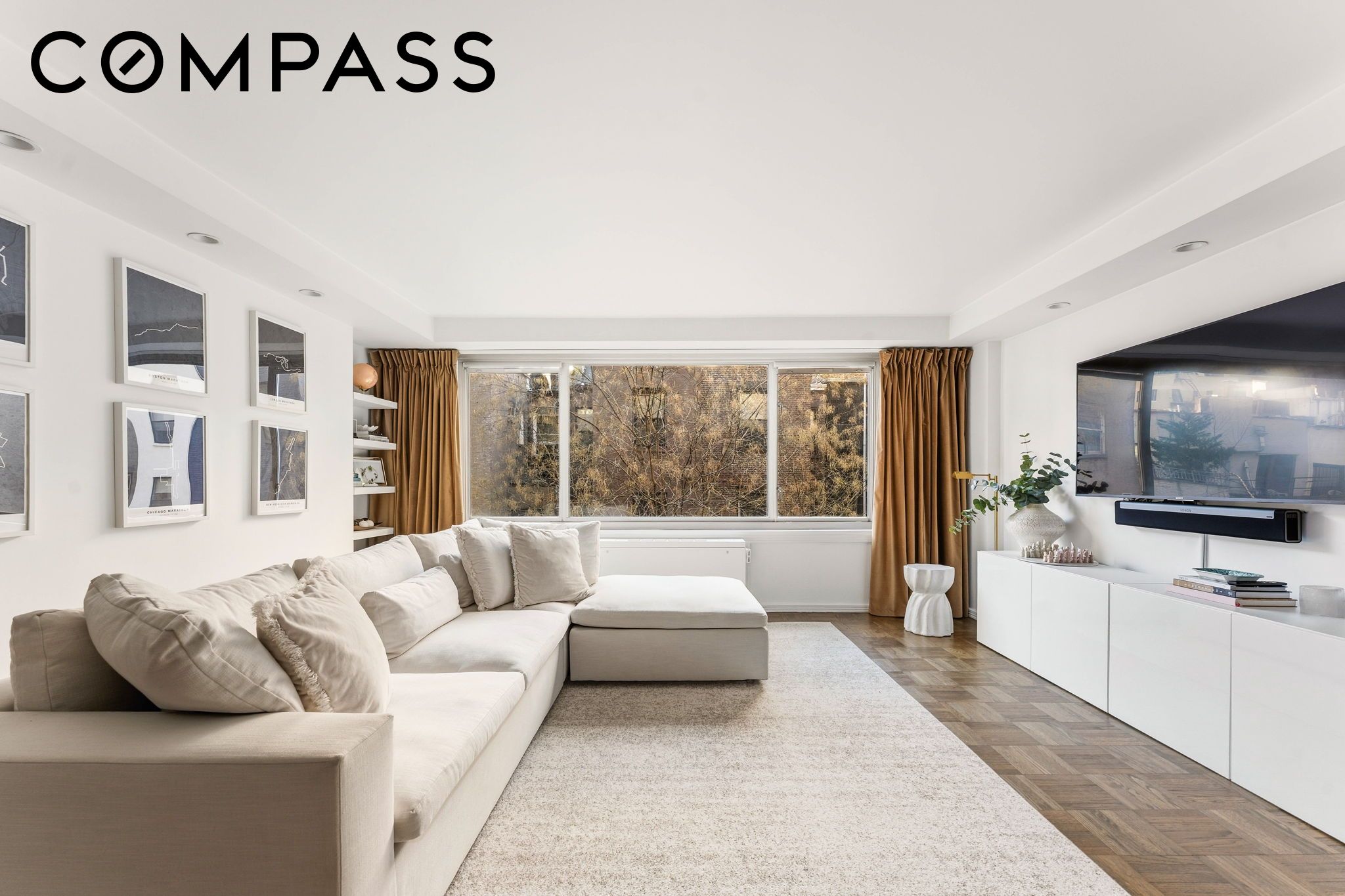 Living room with a cream sectional, wide curtained windows, and parquet flooring.
