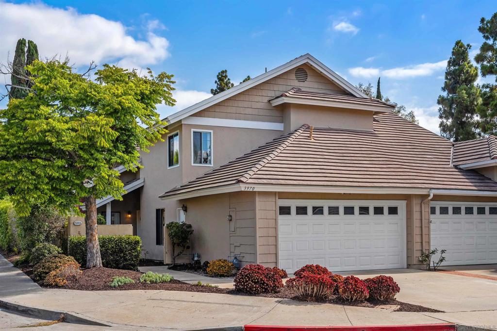 Beige two-story home with tiled roof, double garage, and landscaped flower beds.