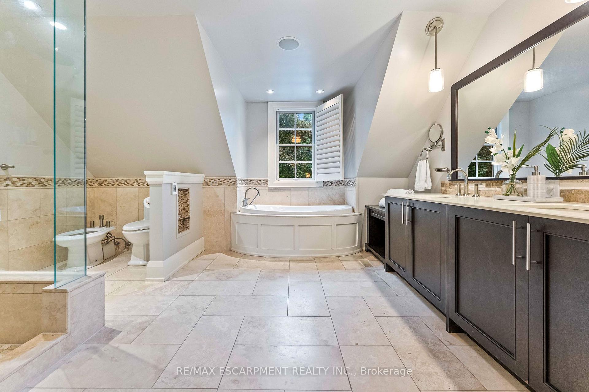 Bathroom with a corner soaking tub, glass shower, and long dark vanity beneath a sloped ceiling.