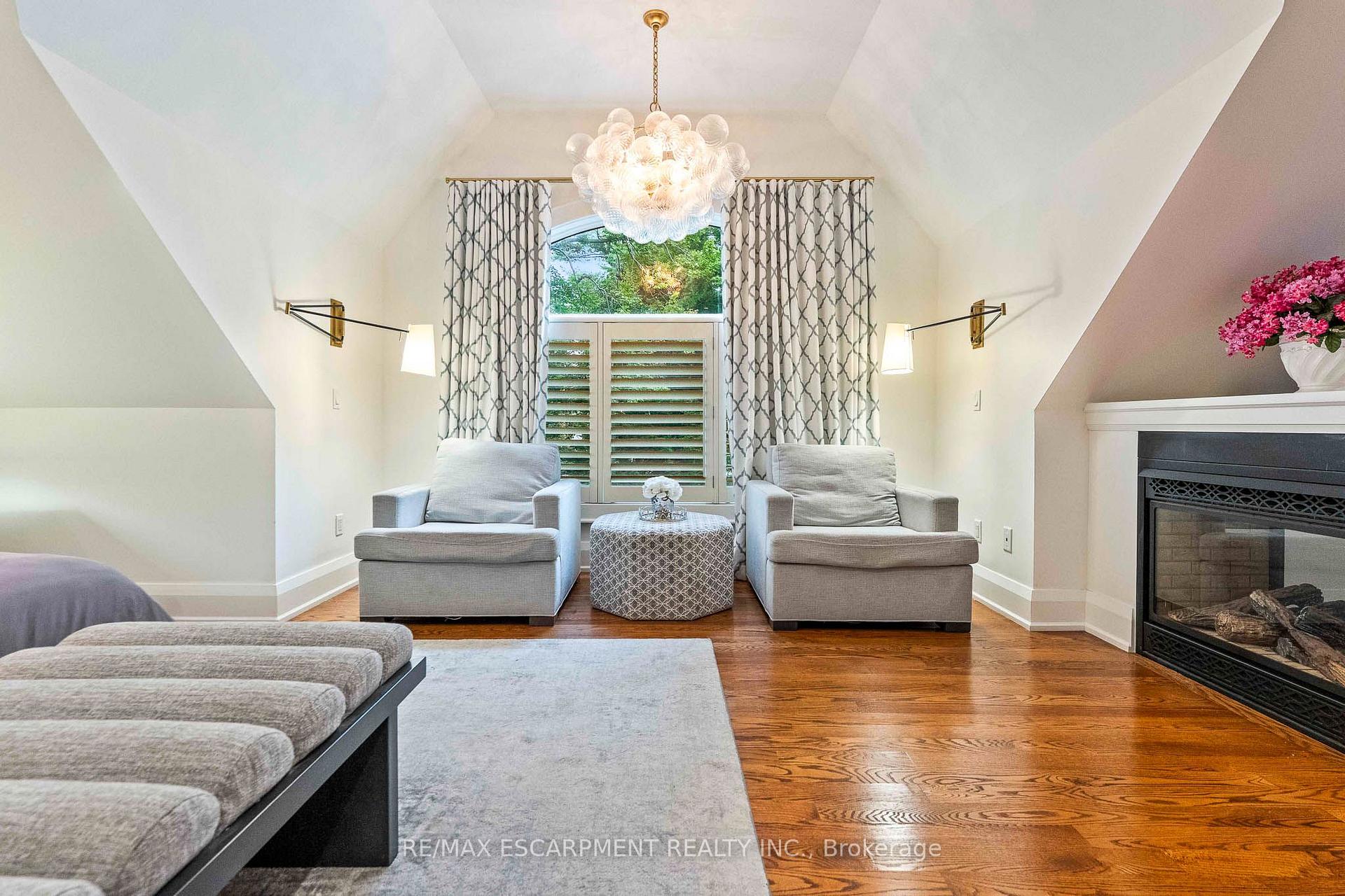 Bedroom sitting area with vaulted ceiling, fireplace, armchairs, and shuttered window.