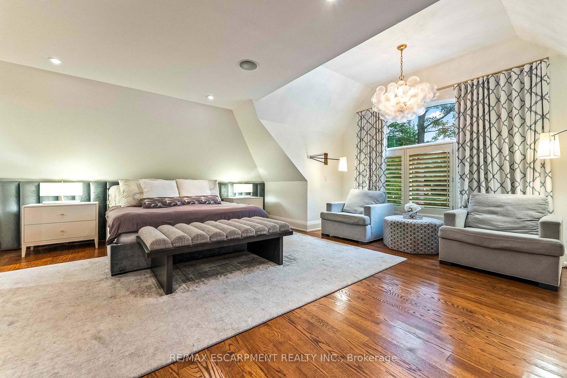 Staged bedroom with a large bed, upholstered bench, gray armchairs, and a chandelier.