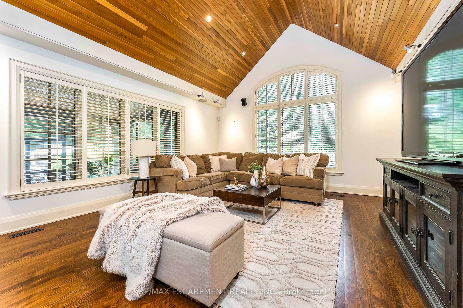 Living room with a vaulted wood ceiling, arched window, sectional sofa, and hardwood floors.
