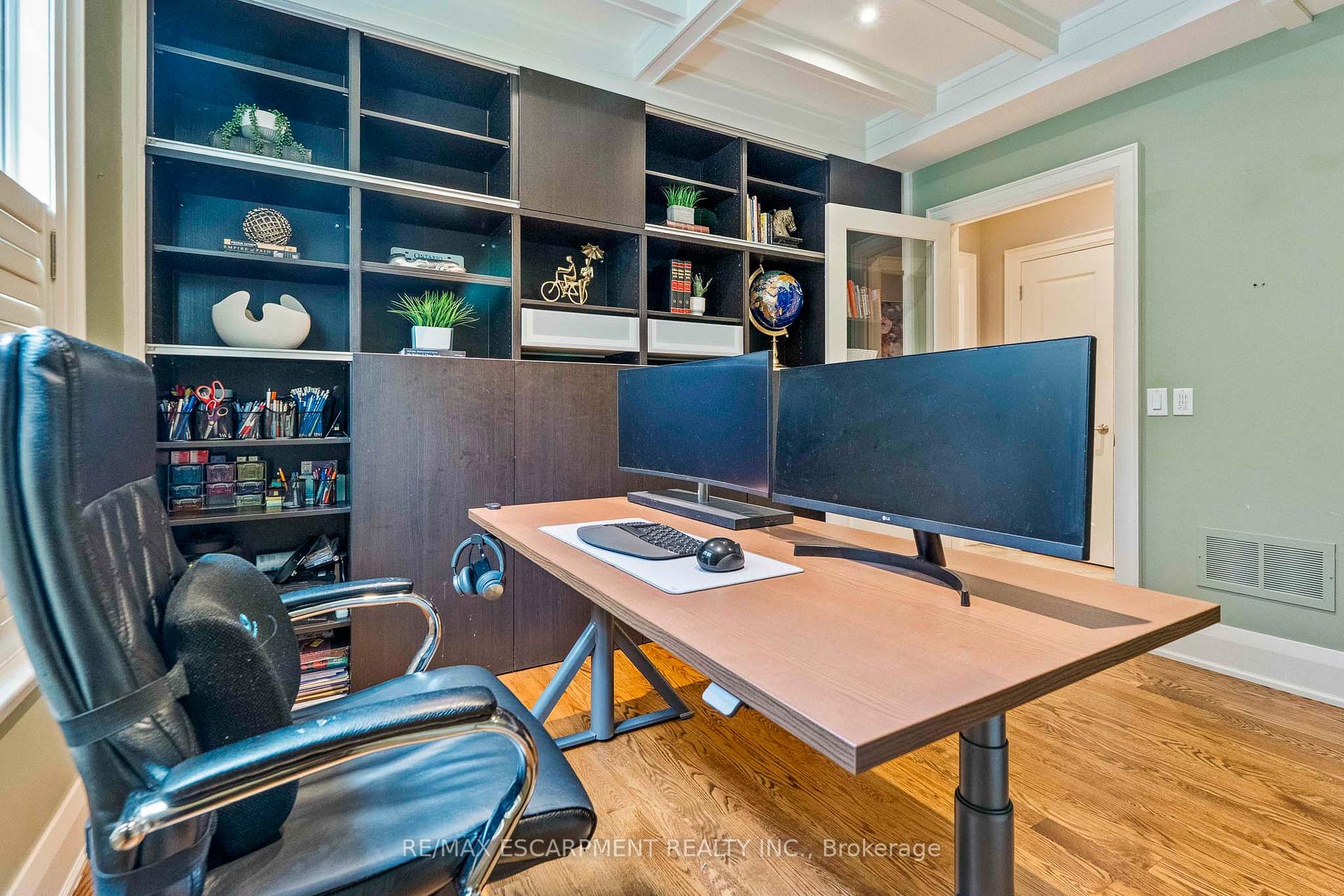 Home office with a wide desk, dual monitors, leather chair, and built-in shelves.