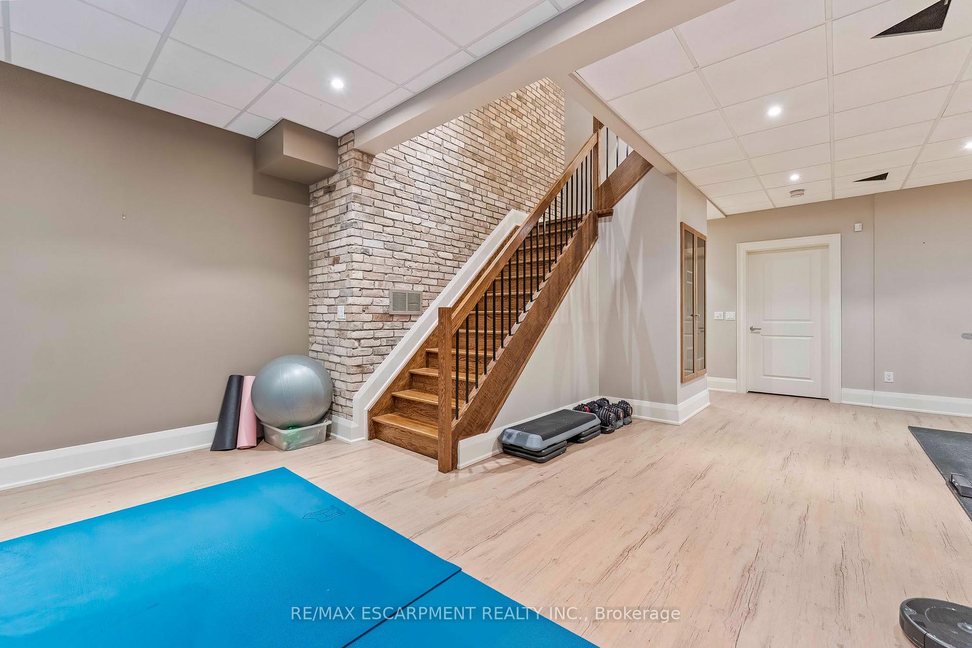 Basement exercise room with a blue workout mat and wooden staircase beside a white brick wall.