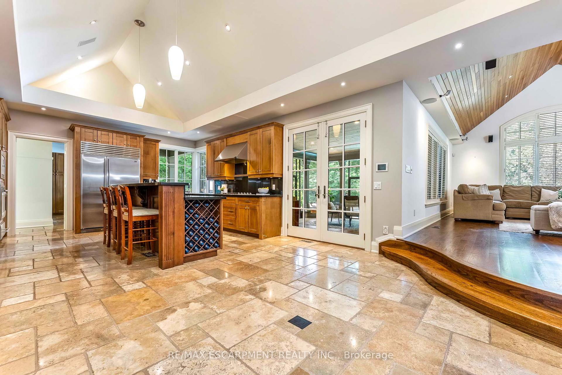 Kitchen and living area with wood cabinetry, wine storage, stone tile floors, and a vaulted ceiling.