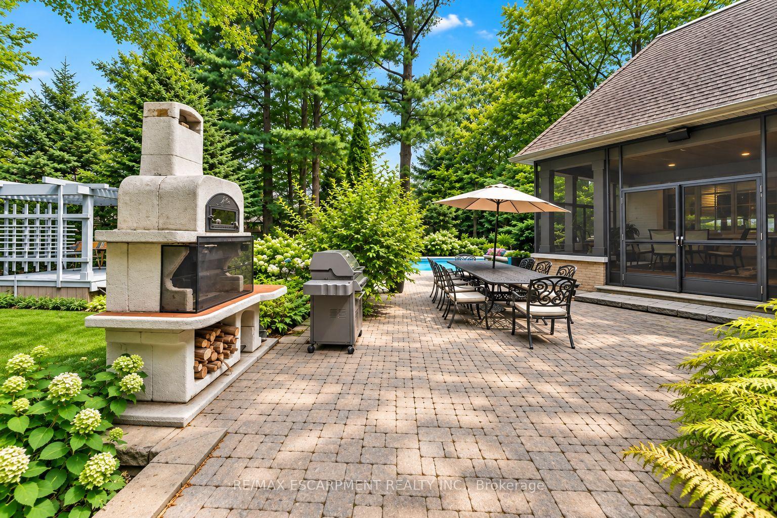 Backyard patio with a stone fireplace, barbecue, and umbrella-covered dining table beside a screened porch.