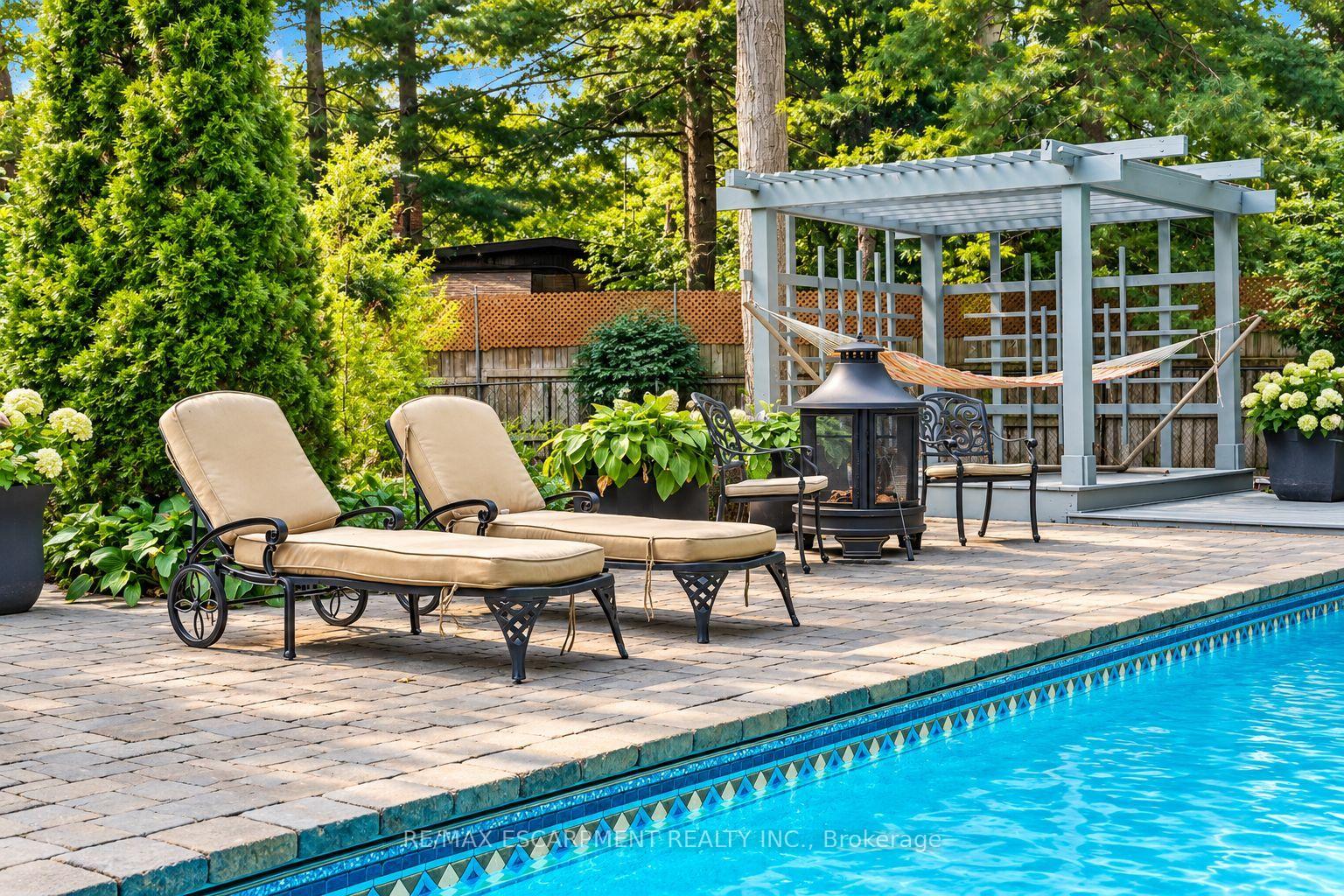 Backyard pool patio with cushioned chaise lounges, a fire pit, and a pergola with a hammock.