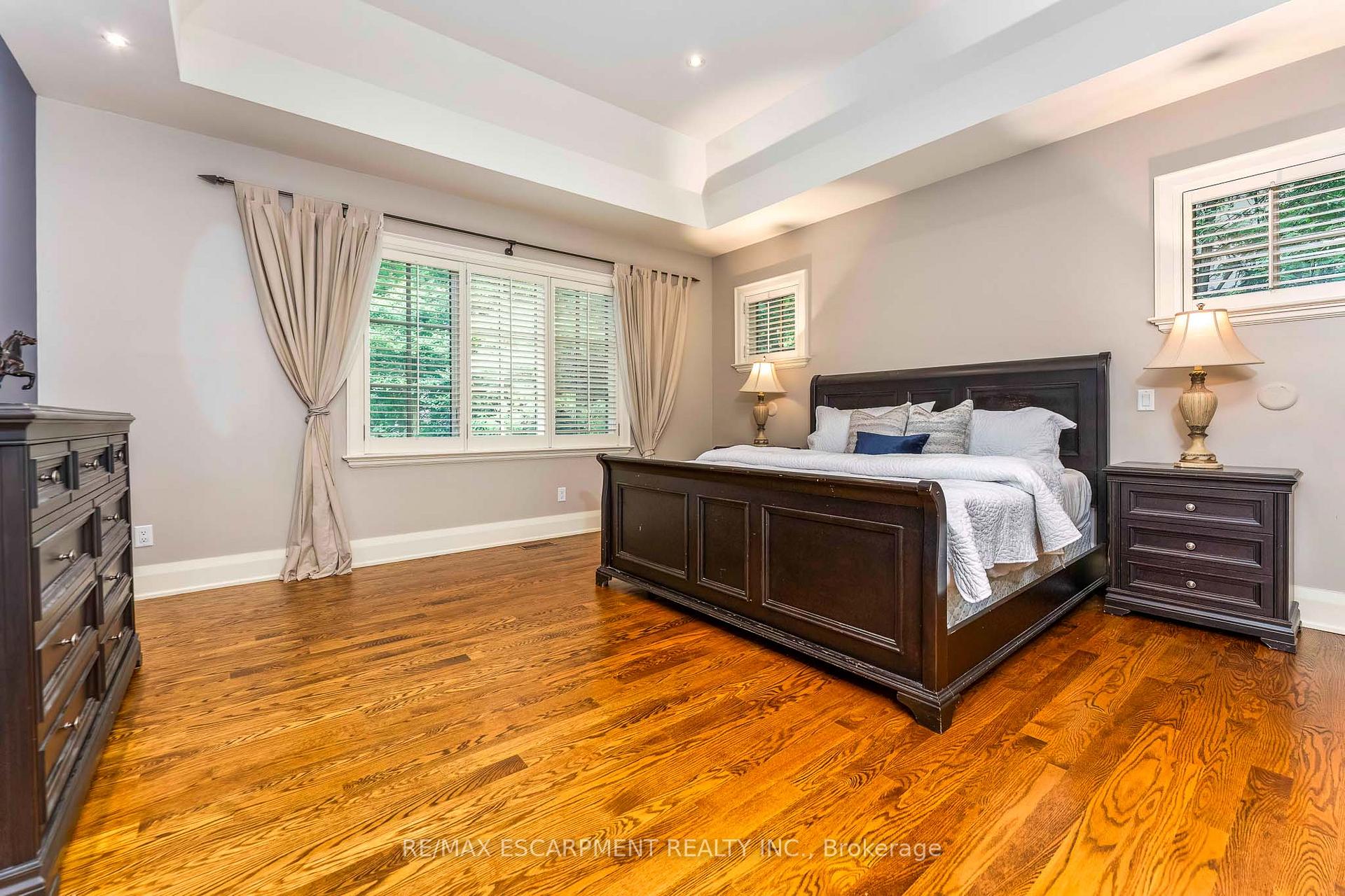 Furnished bedroom with a dark wood bed, wide curtained windows, and polished hardwood floors.