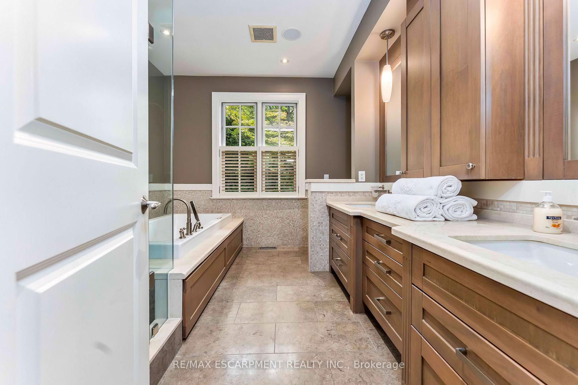 Bathroom with a glass-enclosed tub, double vanity, warm wood cabinetry, and rolled white towels.