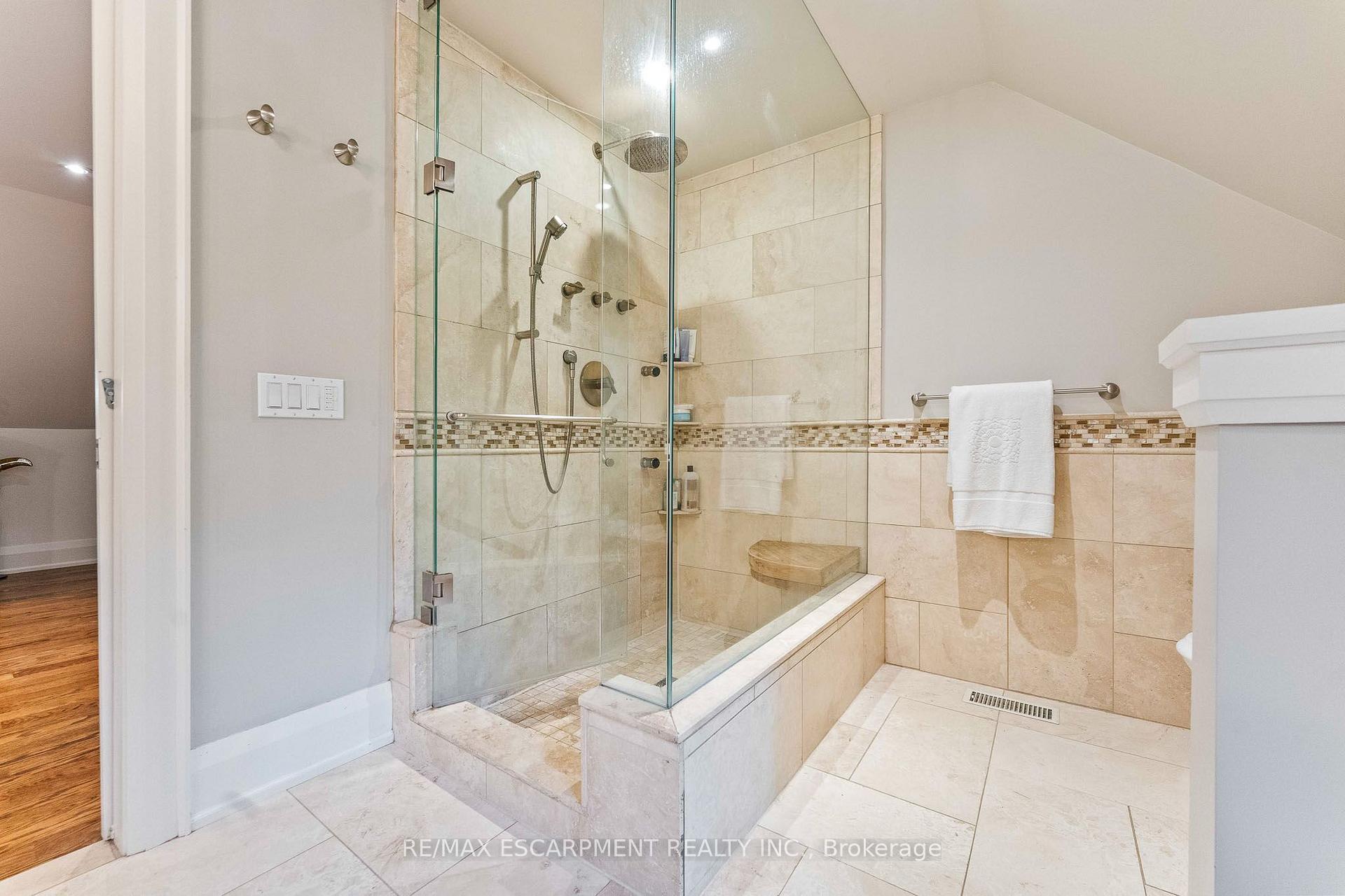 Bathroom with a glass-enclosed tiled shower, tub, and mosaic accent band.