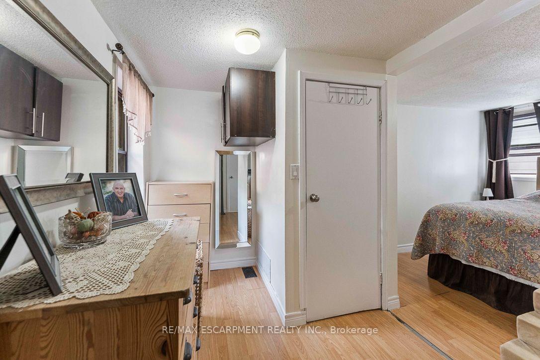 Bedroom with a wooden dresser, dark wall cabinets, and a bed beside a curtained window.